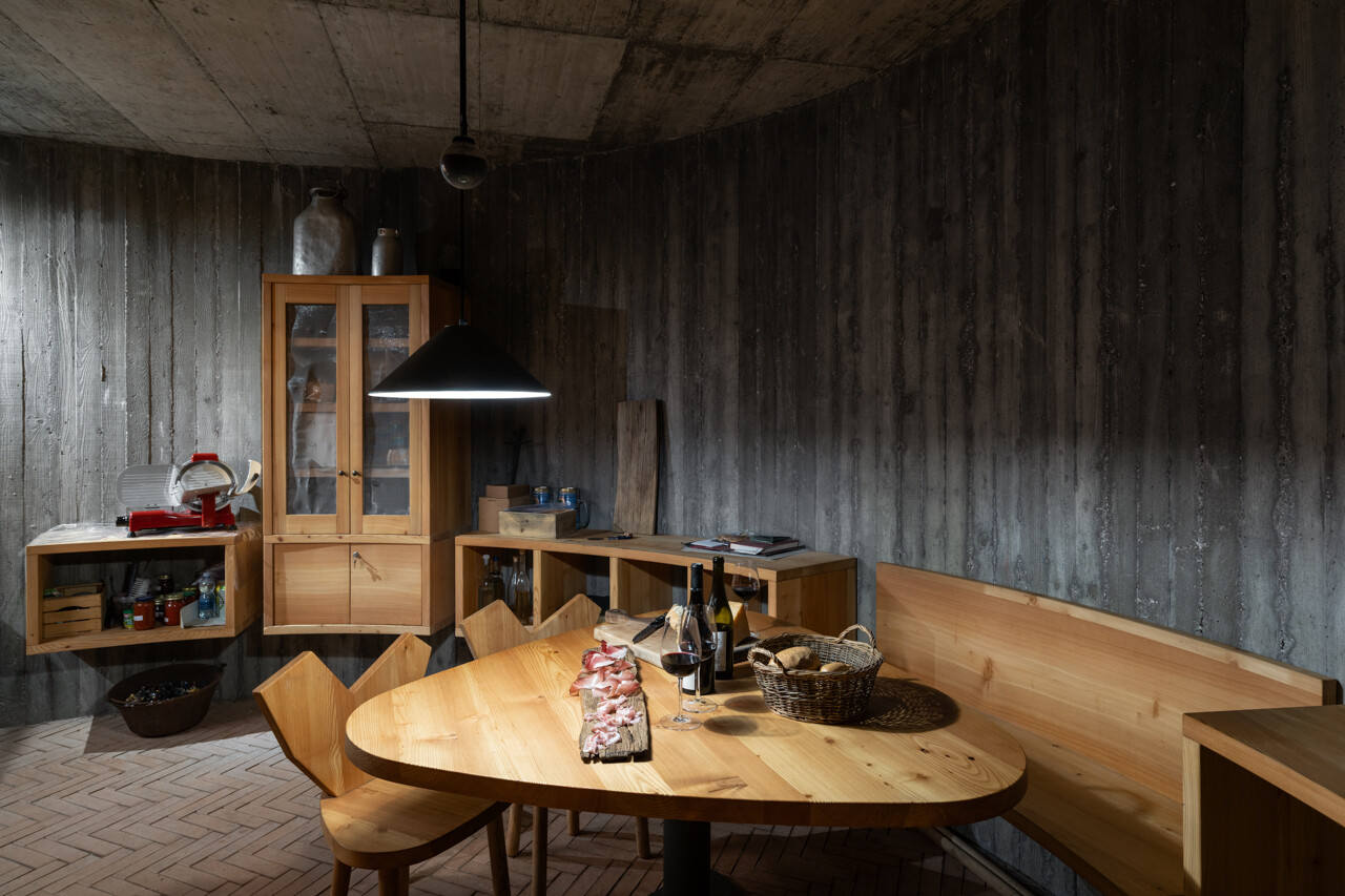 An underground wine cellar with curved concrete walls and brick floors anchors the home to land and memory.