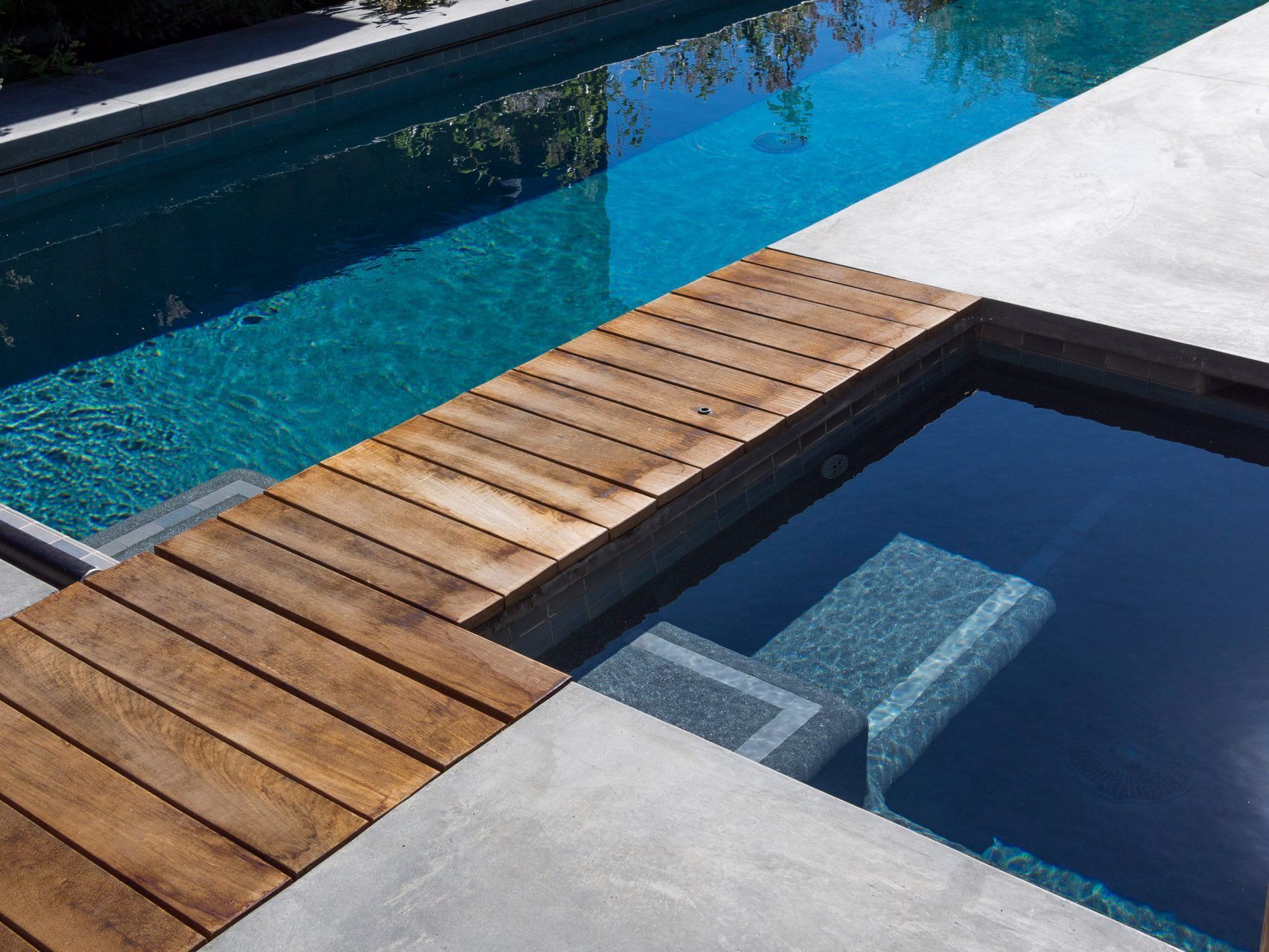 A wooden walkway connects the pool and spa, creating a seamless flow through the backyard.