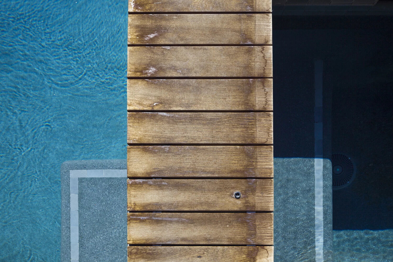 A wooden walkway connects the pool and spa, creating a seamless flow through the backyard.