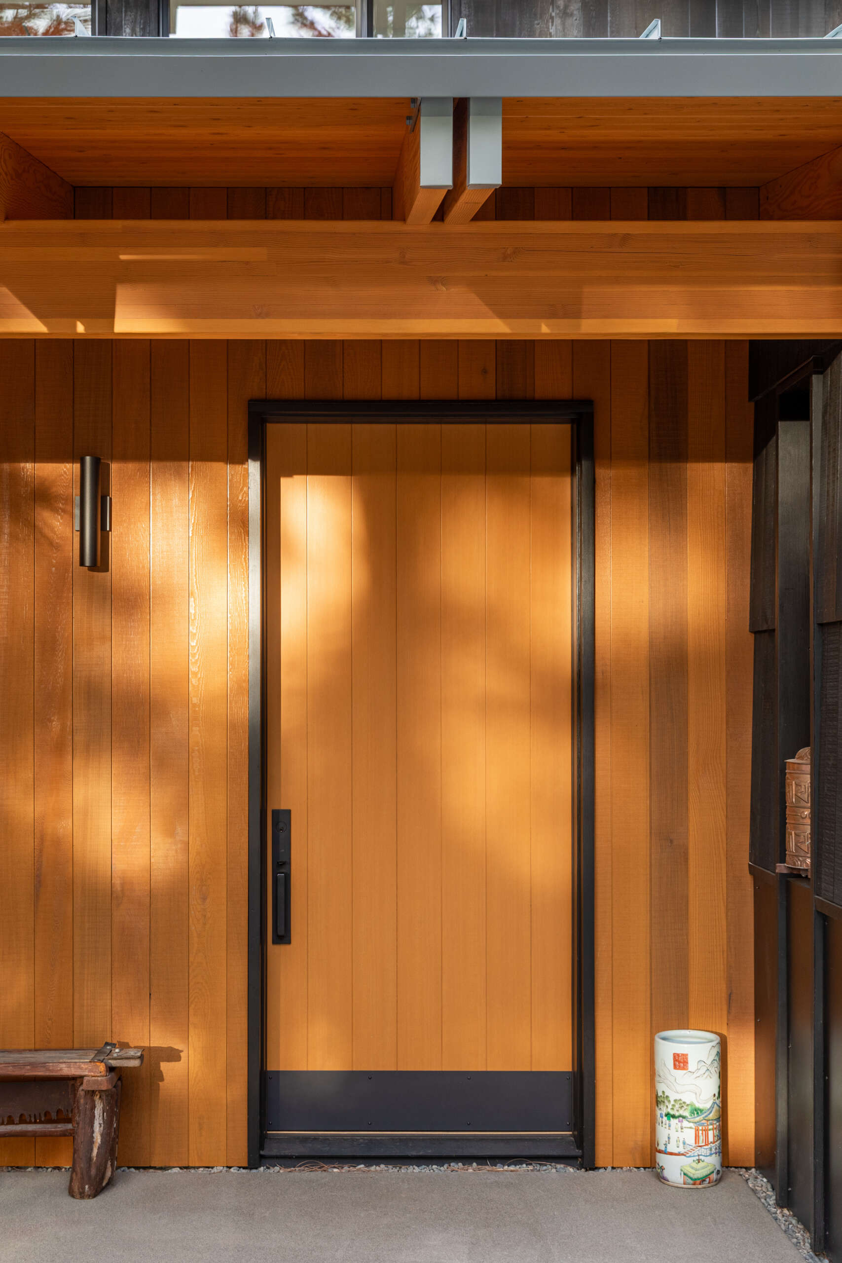 Charcoal wood siding, warm timber accents, and a simple gravel approach create a welcoming arrival that feels grounded in the surrounding mountain landscape.