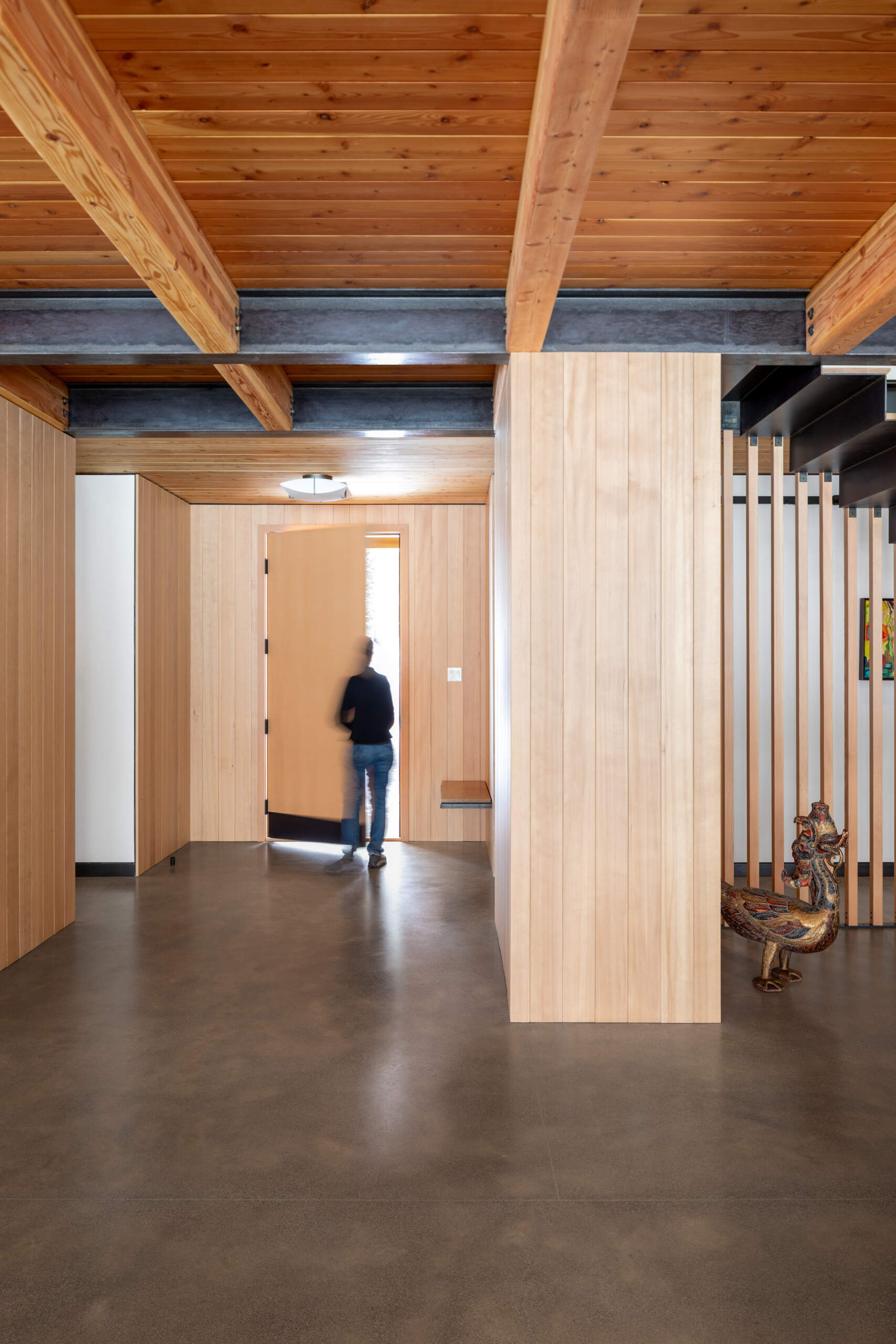 A calm, functional entryway defined by pale wood walls, black steel details, and polished concrete floors, designed to handle daily life with ease and intention.