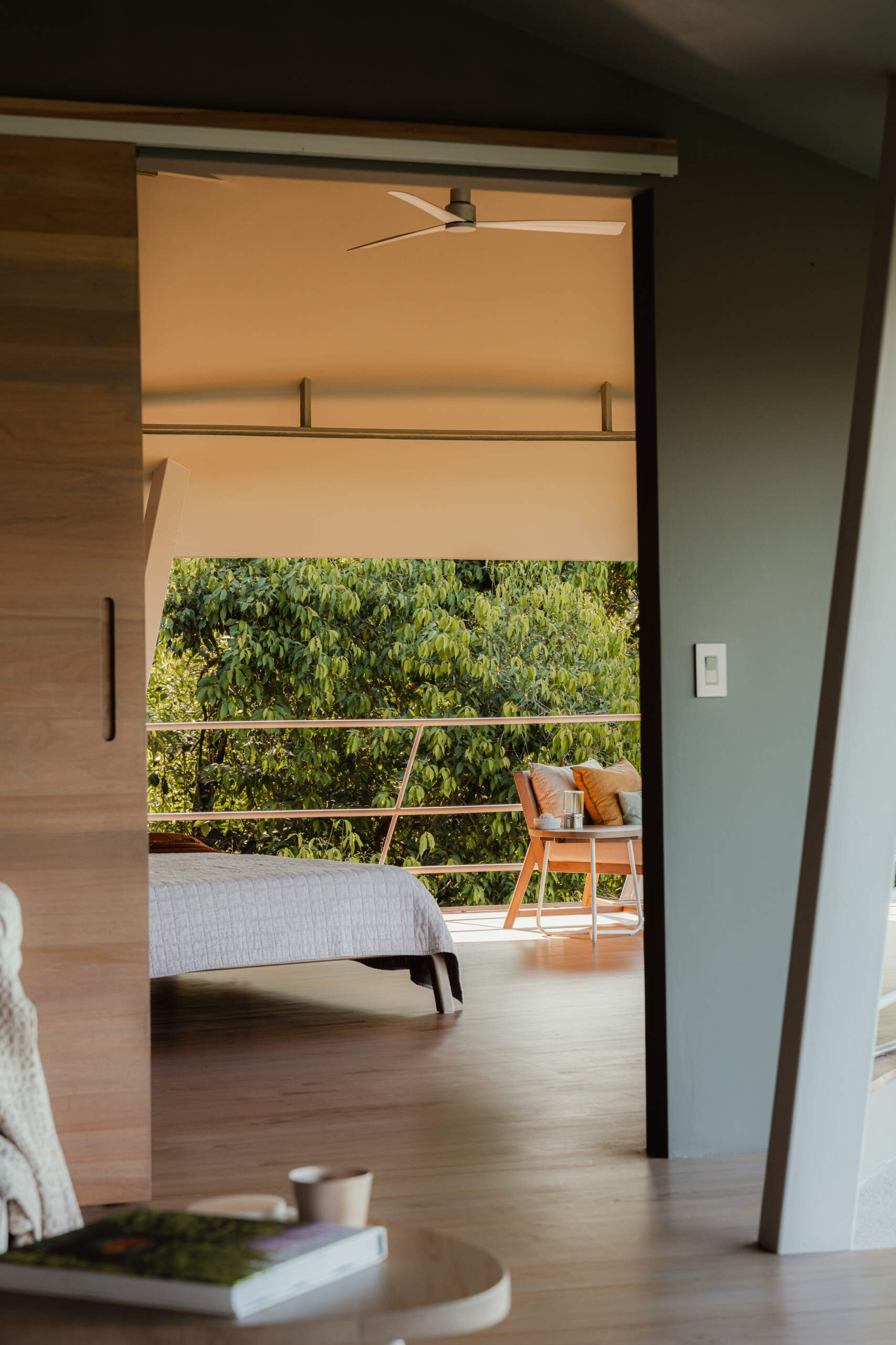 A curved open air bedroom where the sweeping roofline and angled supports frame uninterrupted views of forest and ocean. The low timber bed and minimal furnishings keep the focus on light, air, and landscape.
