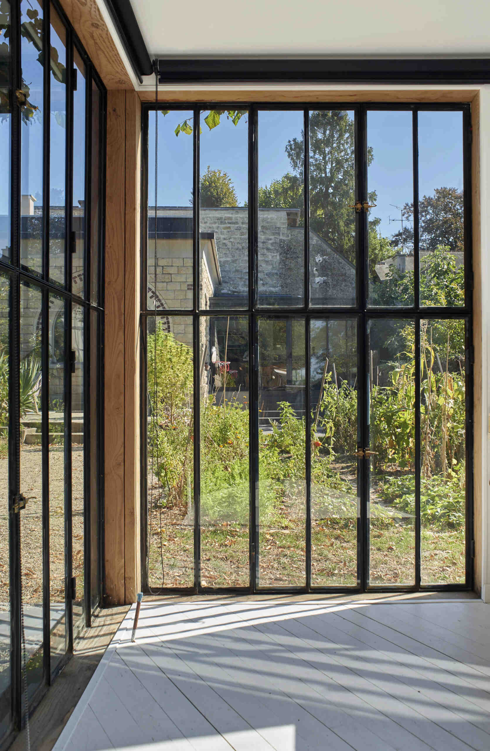 Black-framed windows are positioned to frame views of the vegetable garden, a 1940s house, and a centennial oak.