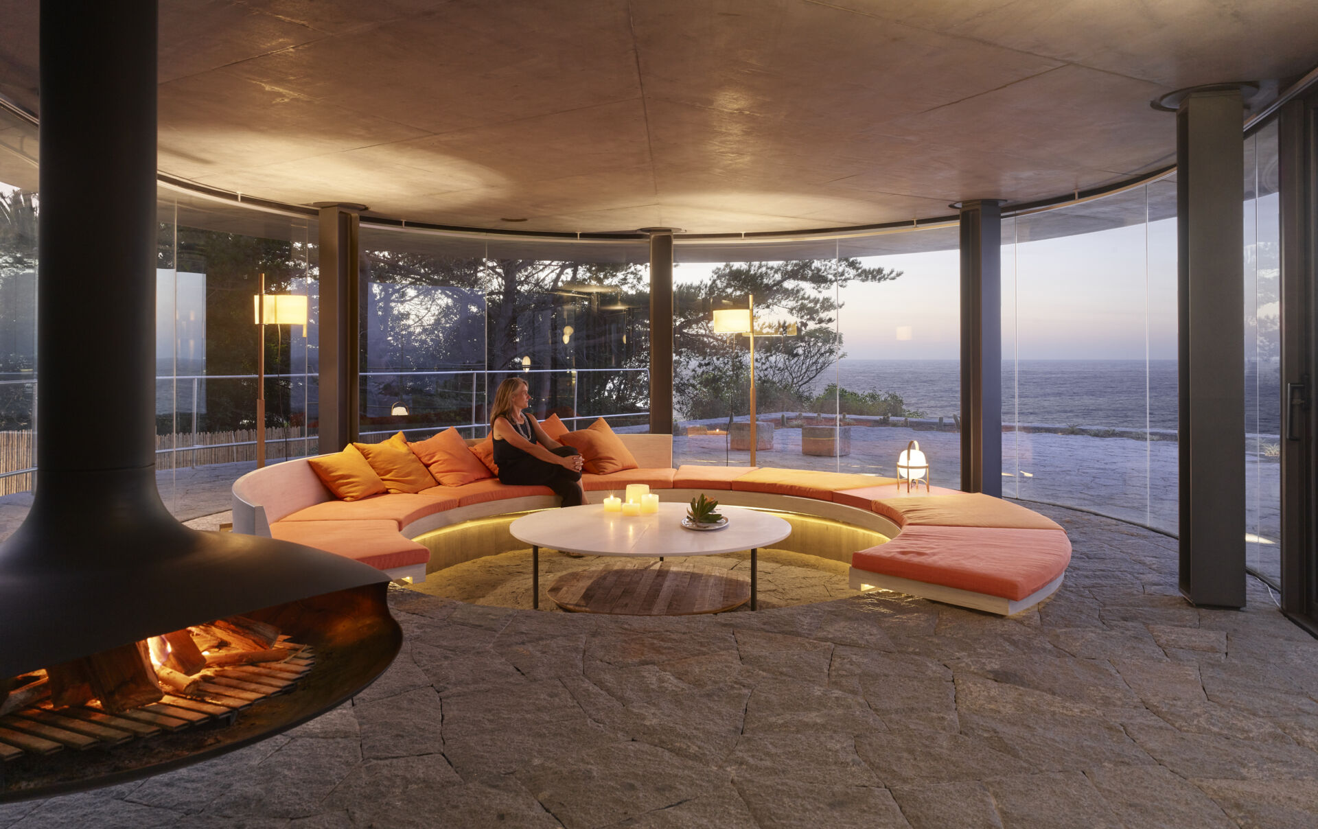 A circular living room with a sunken center and built-in couch, opens fully to the horizon through uninterrupted glass walls.