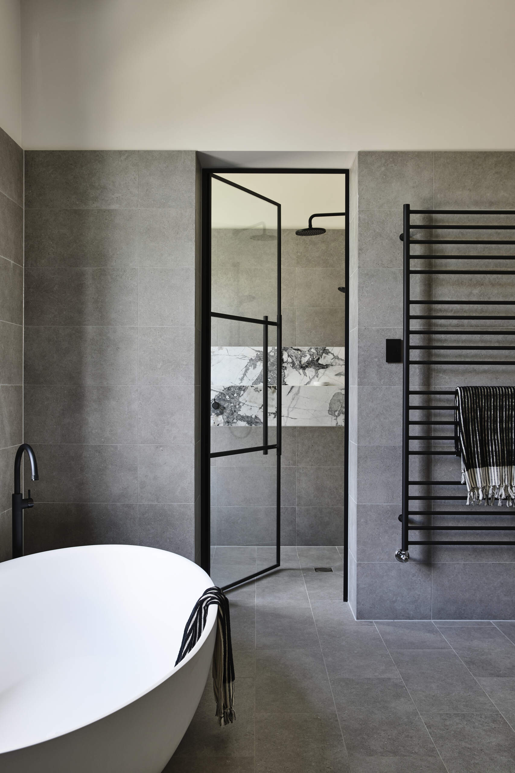 A calm and tailored bathroom wrapped in charcoal-gray tile with a floating dark wood vanity and white marble tops. Black fixtures and freestanding tubs create a spa-like feel.