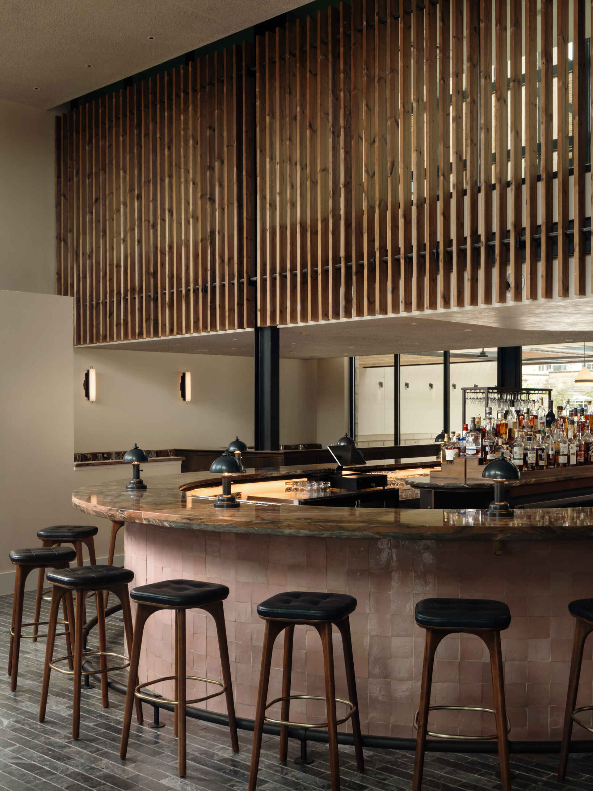 Dining and bar areas flow from this same palette, mixing plaster walls, patterned banquettes, dark wood tables, and a softly lit bar finished in stone, tile, and timber. Together, the spaces feel cohesive, relaxed, and designed for unhurried moments rather than quick arrivals.