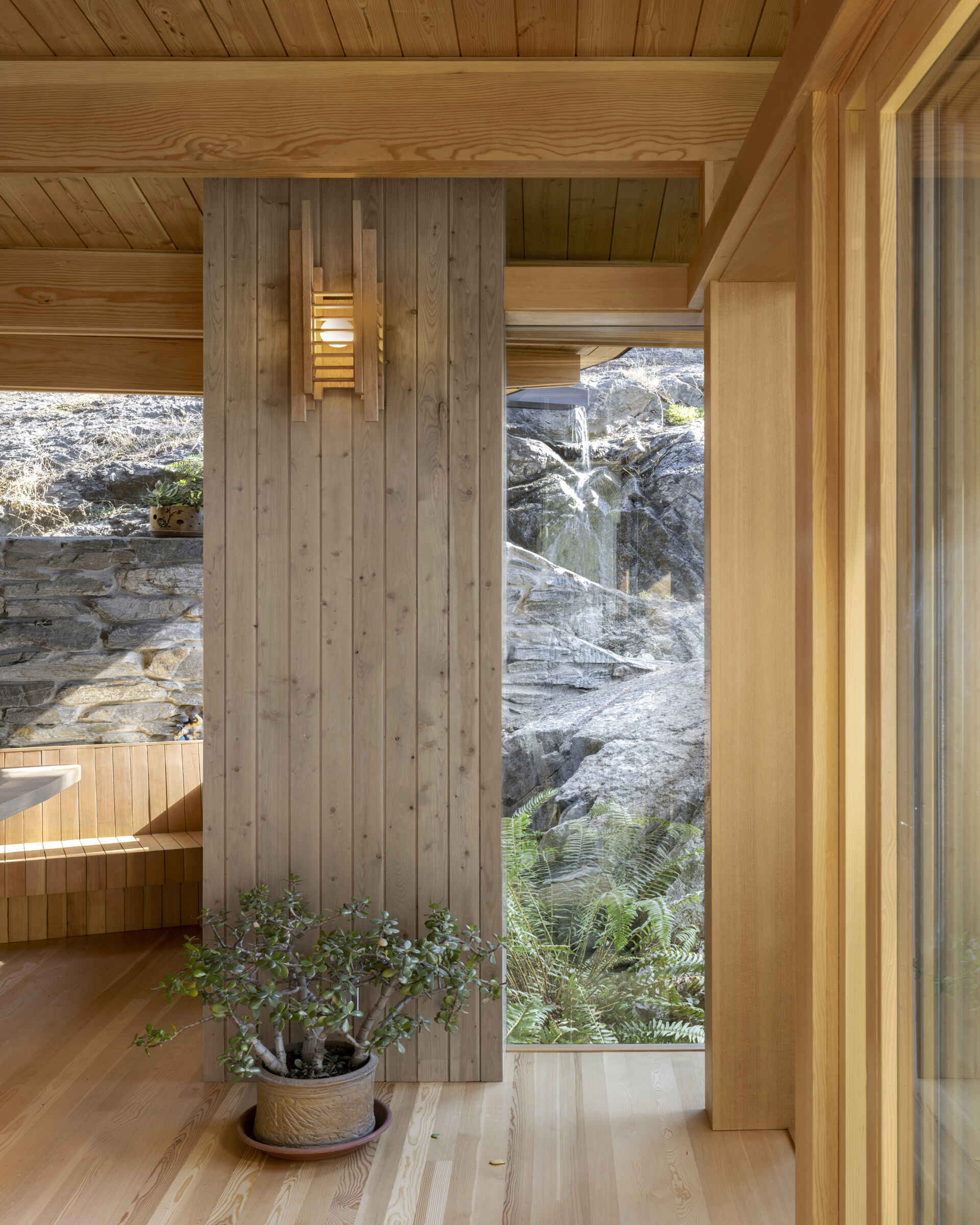 Inside, the stone wall becomes a backdrop for daily life and work. Reflected daylight warms faces during virtual meetings, while the textured surface provides visual calm. 