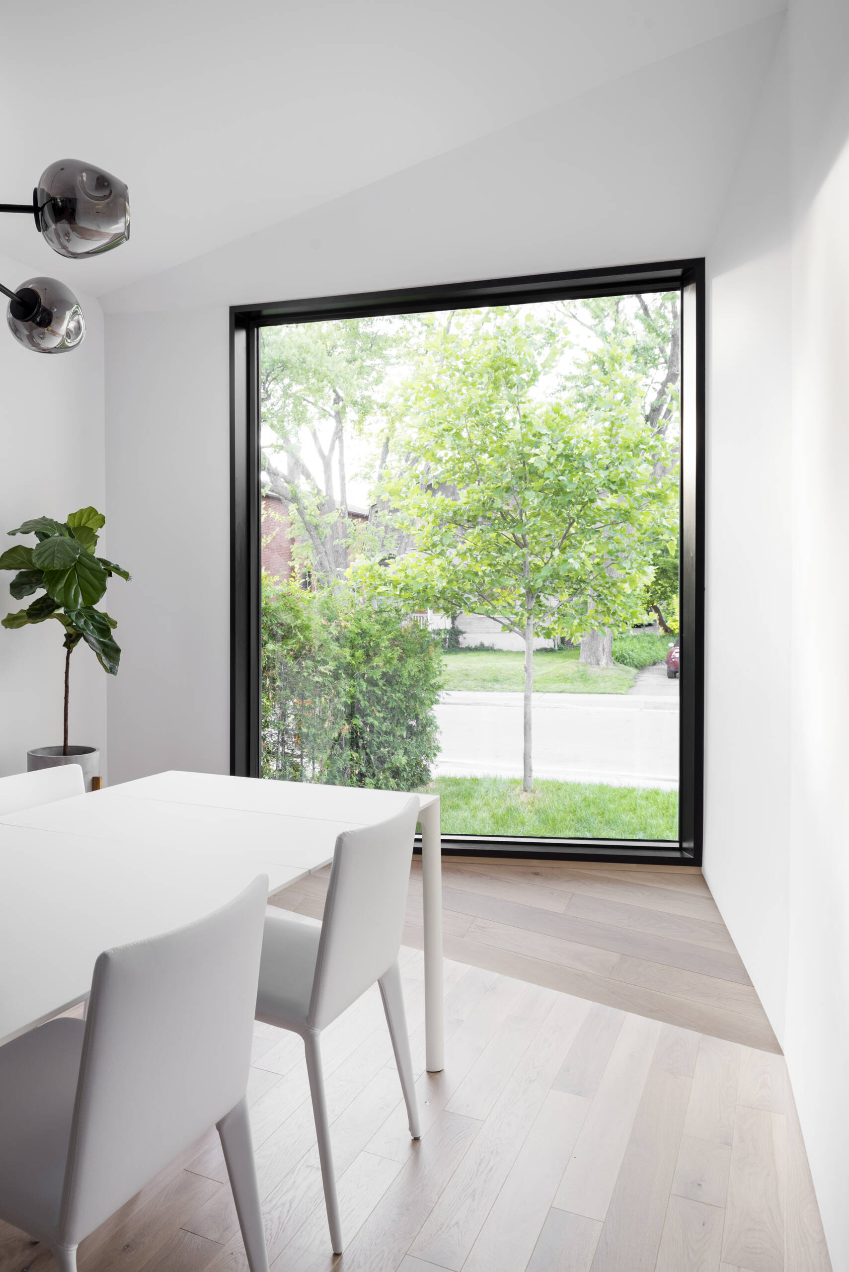 A minimalist white dining setup sits beside a large picture window, drawing daylight into the heart of this modern Toronto home.