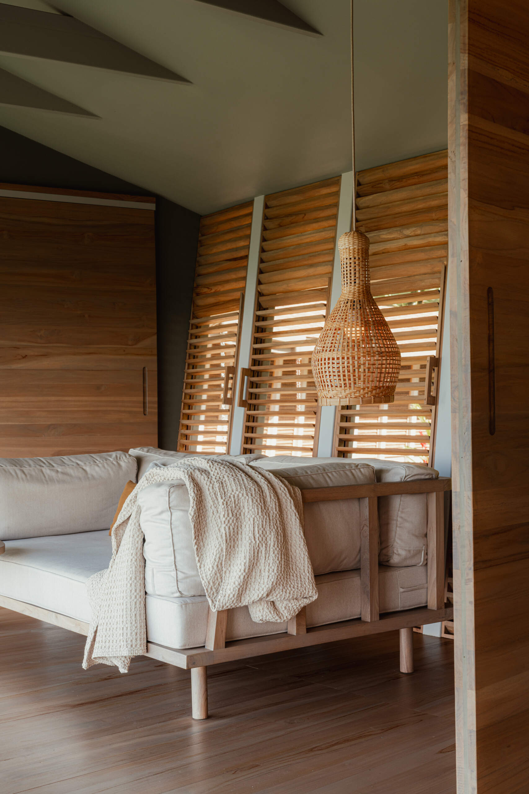 The living room balances structure and softness through a solid wood frame sofa paired with neutral cushions and tactile throws, all grounded by rich timber flooring.