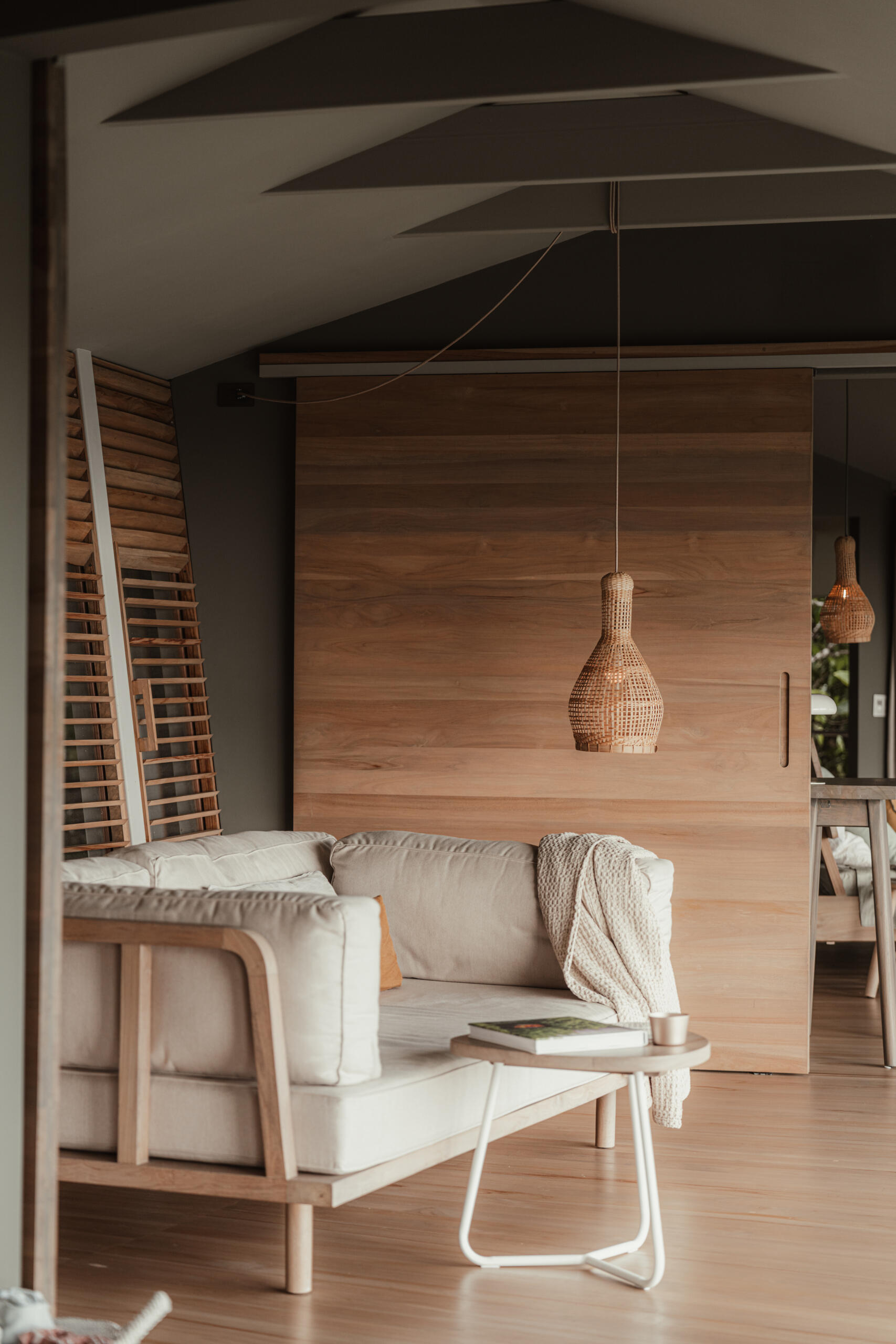 The living room balances structure and softness through a solid wood frame sofa paired with neutral cushions and tactile throws, all grounded by rich timber flooring.