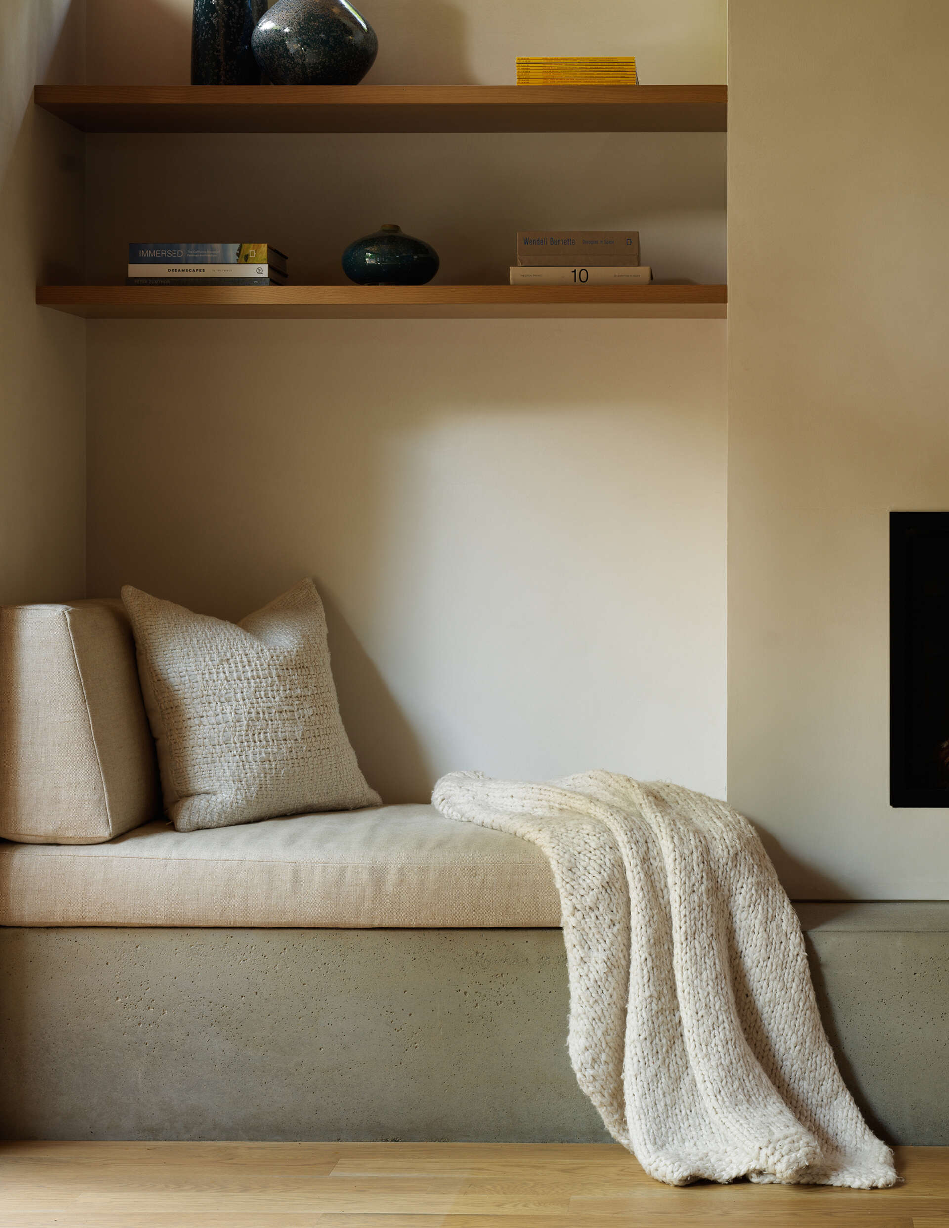 The living area is anchored by a wood-burning fireplace beneath a soft loft, offering warmth and focus. Expansive windows draw in light and frame views of moss-covered rockery, ferns, and native trees. A cozy seating nook lets residents enjoy quiet moments while staying connected to the outdoors.