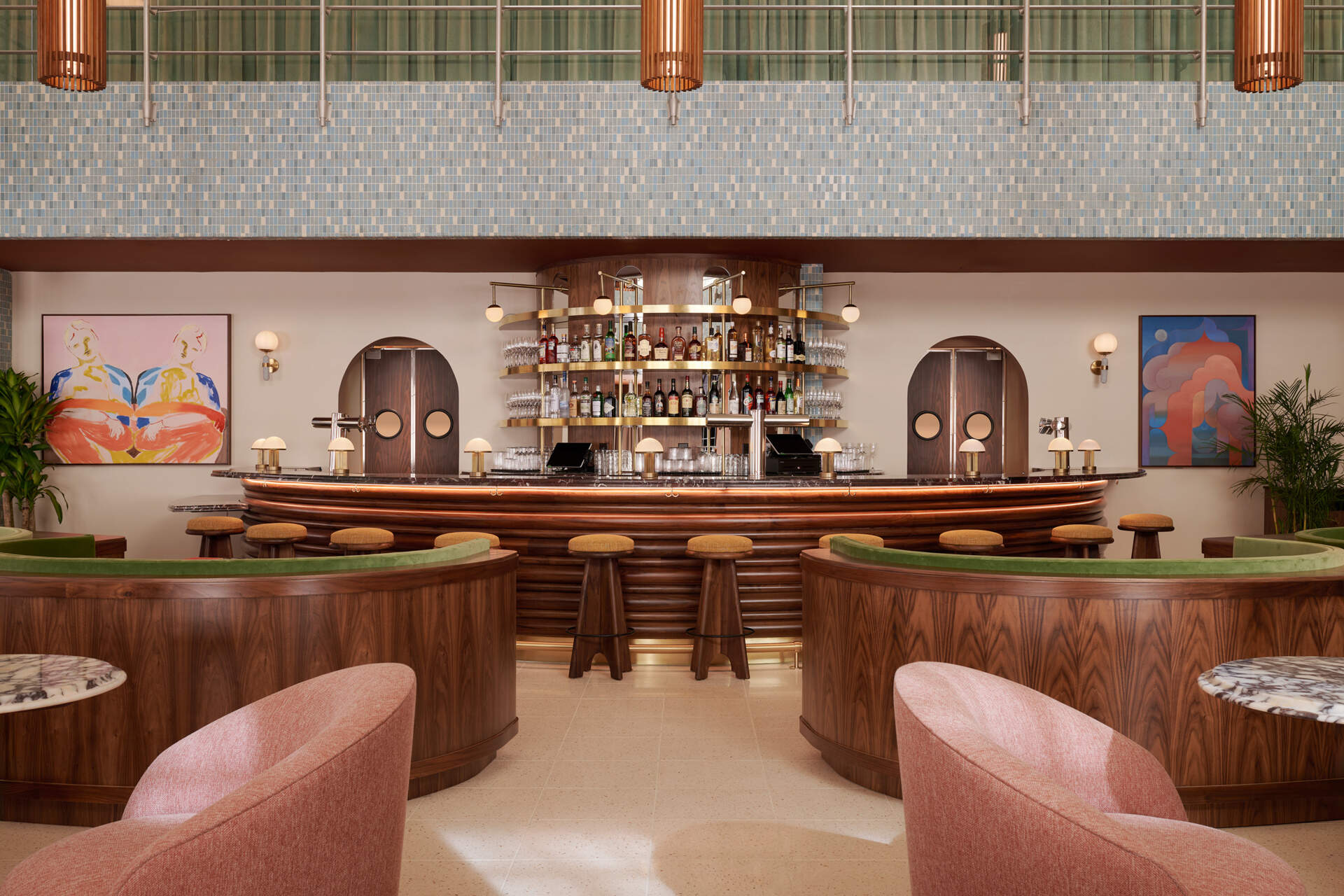 A double heighthotel lobby centers on a sculptural semicircular bar, where restored mosaic tile and mid-century lighting set the tone for gathering.