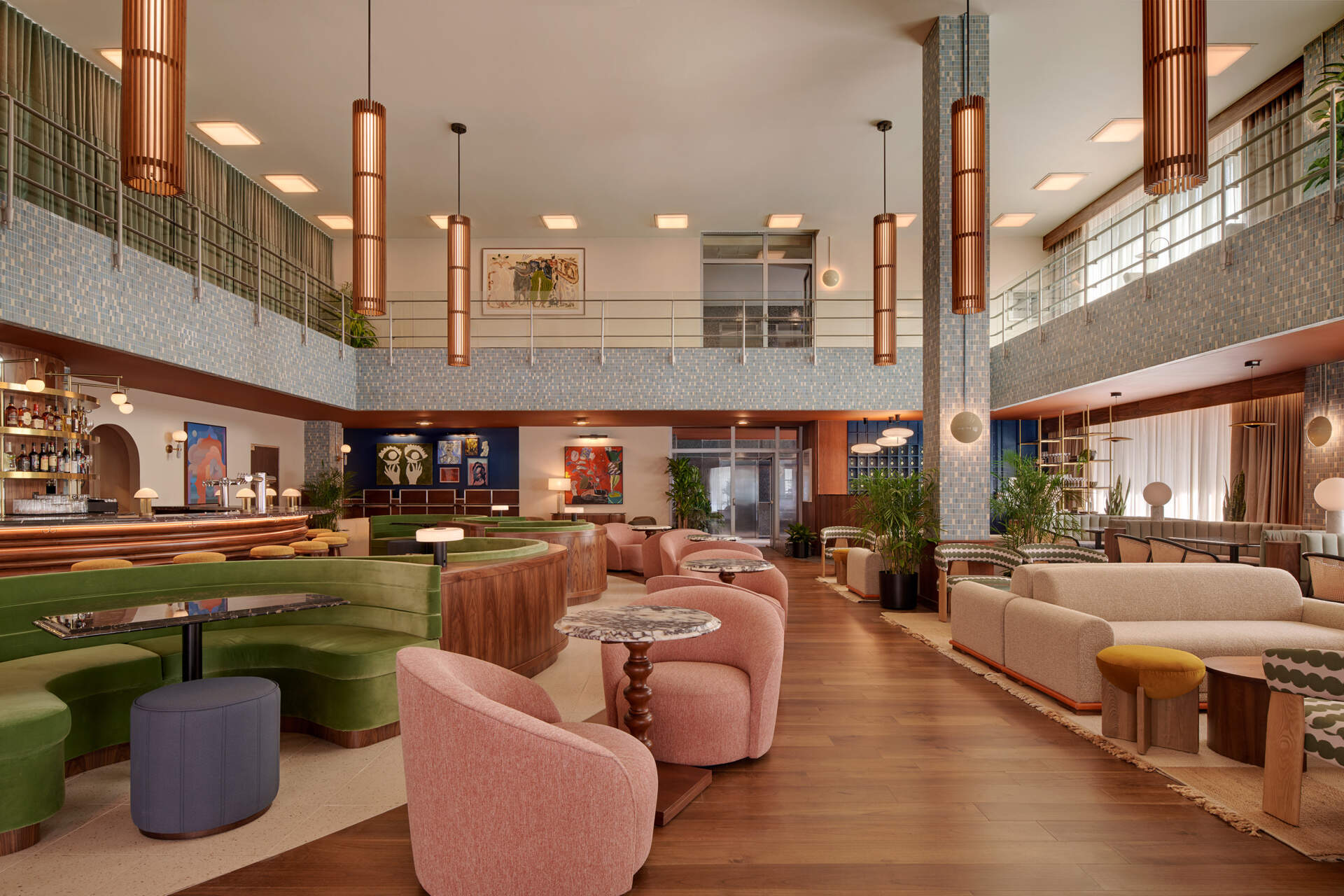 A double heighthotel lobby centers on a sculptural semicircular bar, where restored mosaic tile and mid-century lighting set the tone for gathering.