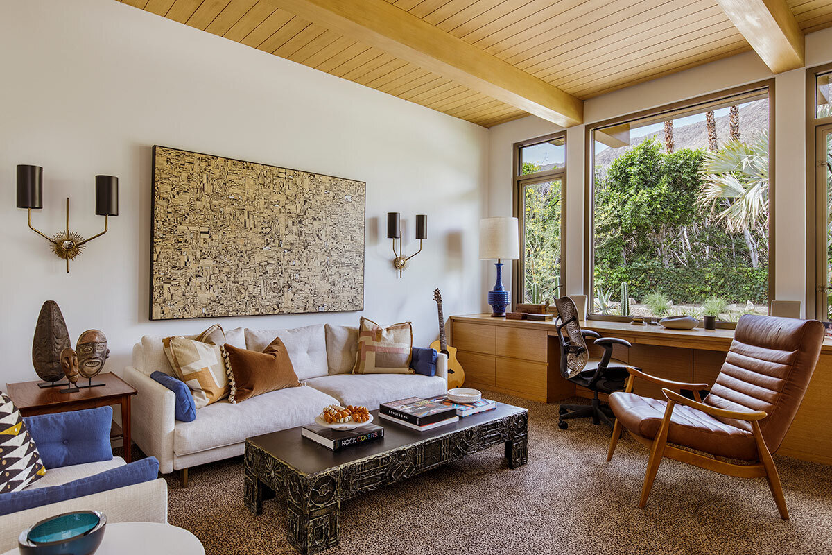A serene home office with a wall to wall desk and a large window framing tree views.