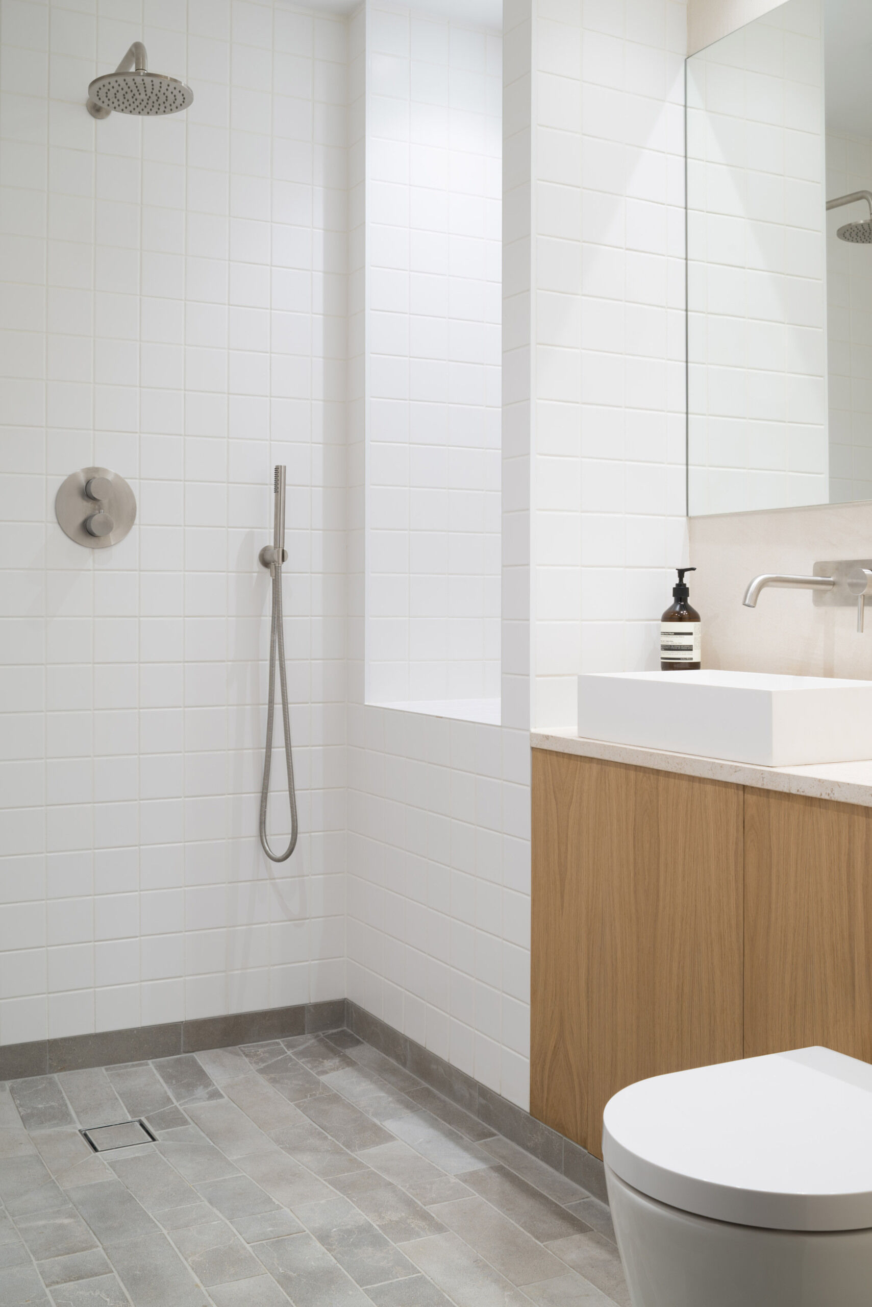 Simple white tiles and grey limestone flooring create a clean and tactile bathroom tucked beside the bedroom.