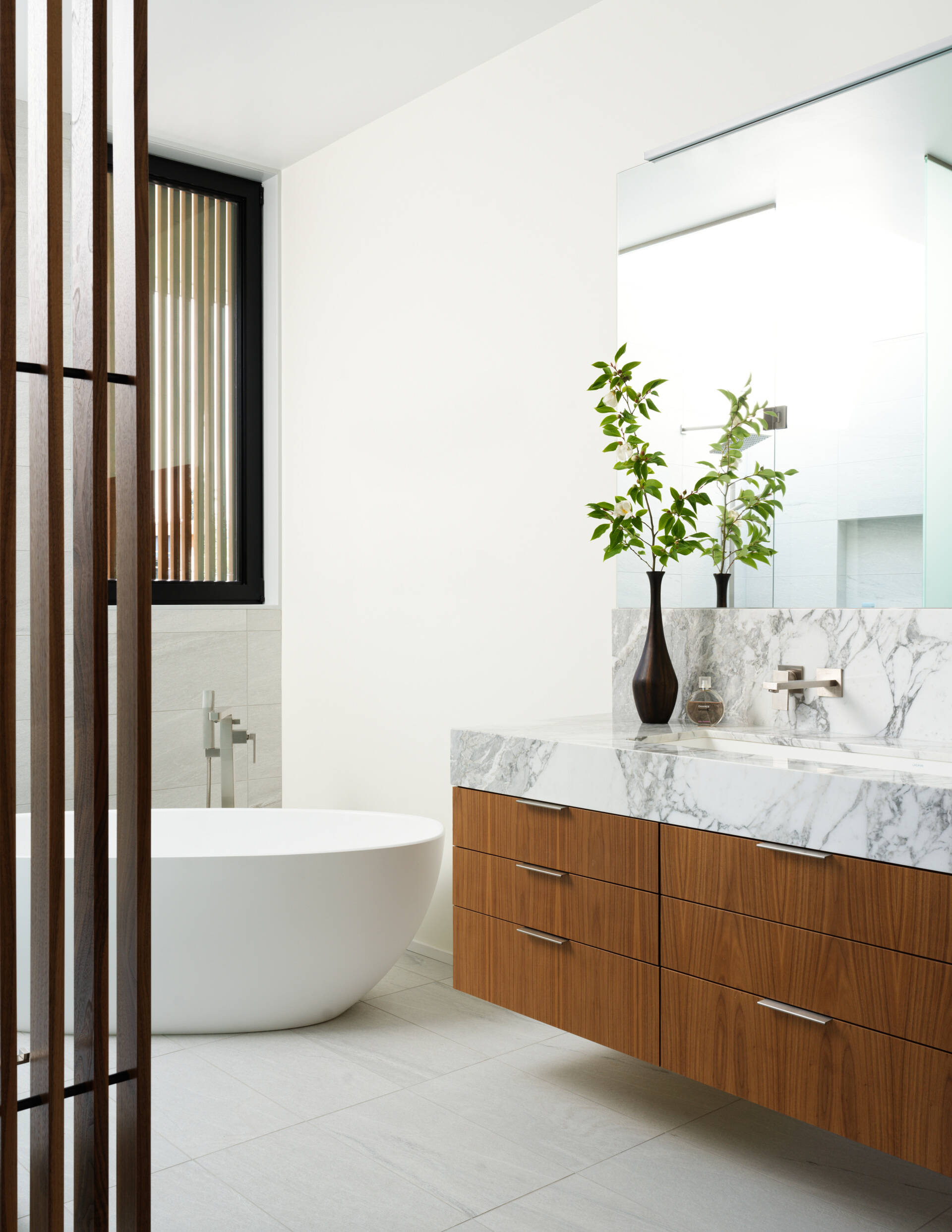 This primary bathroom suite has layered wood screens and minimalist textures to create calm.