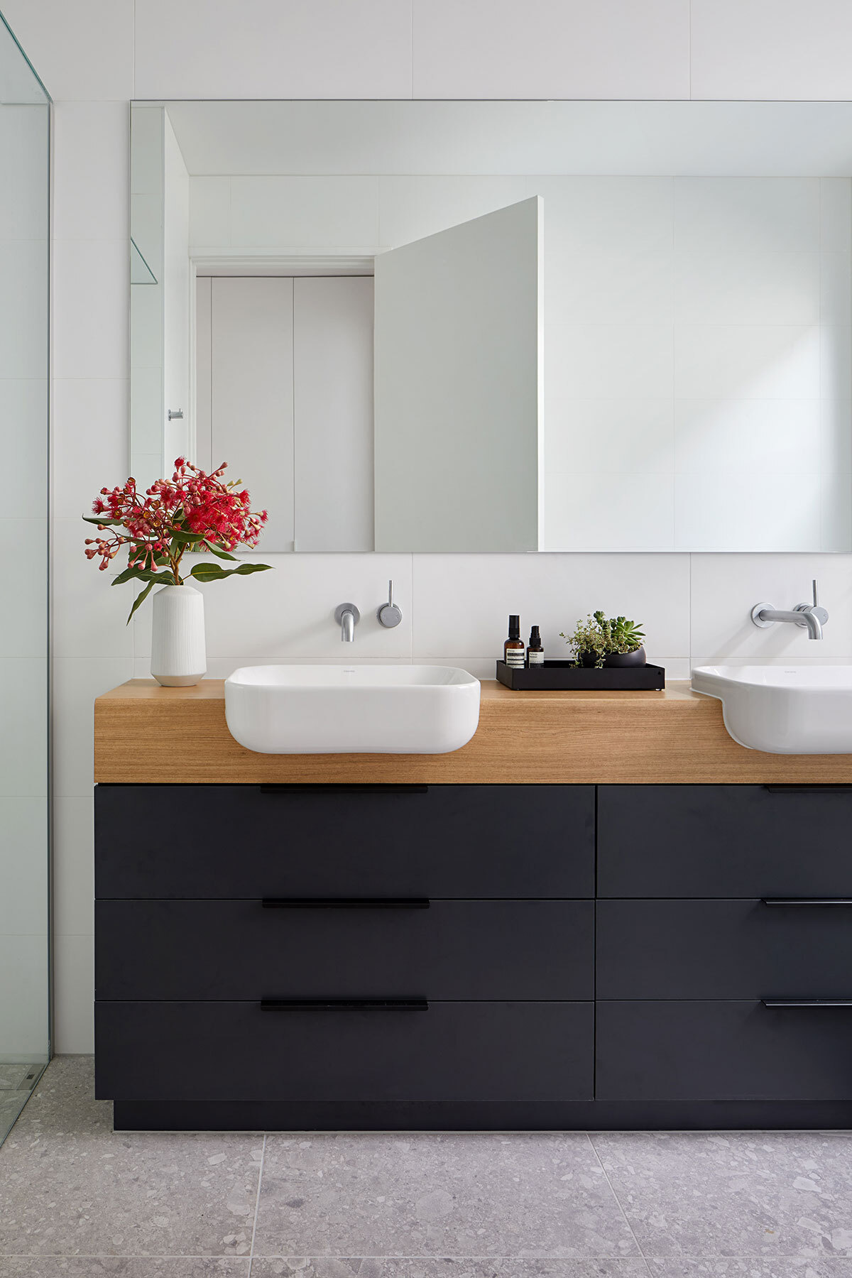 A black and wood vanity contrasts white walls, with a mirror that reflects light throughout the bathroom.