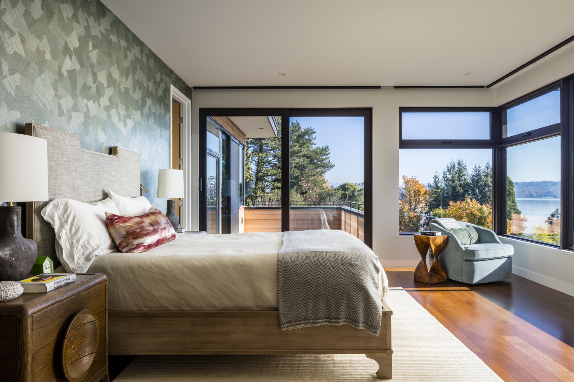 This bedroom with sliding glass doors opens to a small outdoor space, extending the room beyond its walls, while warm wood floors, soft textiles, and patterned accent wall creates a calm setting.