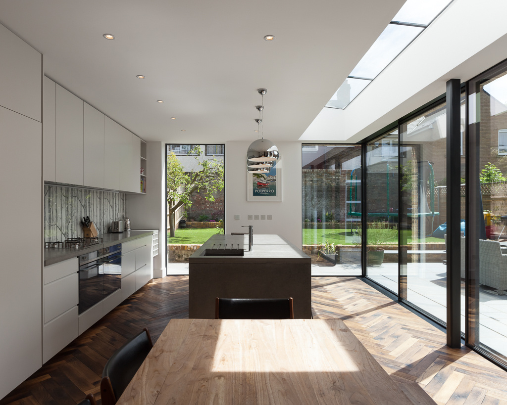 Las puertas correderas de cristal y las paredes de cristal de las esquinas desdibujan los límites entre la cocina y el jardín.