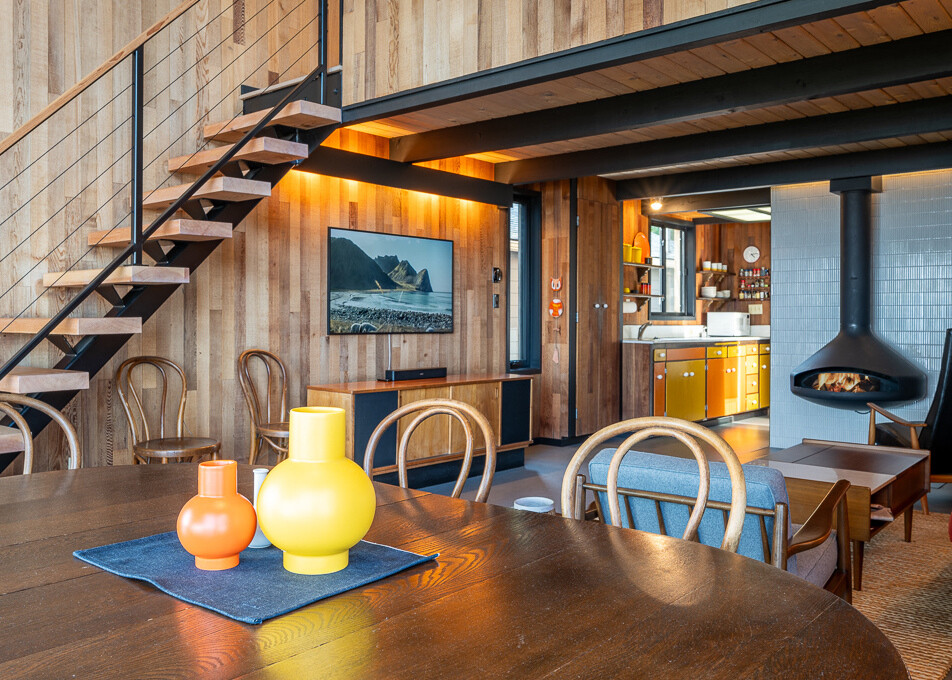 El comedor fluye perfectamente hacia la gran sala. La decoración minimalista y el enfoque en la luz natural crean un telón de fondo tranquilo y acogedor para comidas y reuniones familiares. Gracias a la estructura elevada y al nuevo marco de acero, las vistas de Puget Sound están sin obstáculos. Cuatro ventanas más grandes reemplazaron las antiguas seis pequeñas aberturas, lo que hace que la cabina se sienta conectada con el entorno junto al agua y, al mismo tiempo, garantiza la seguridad contra inundaciones.