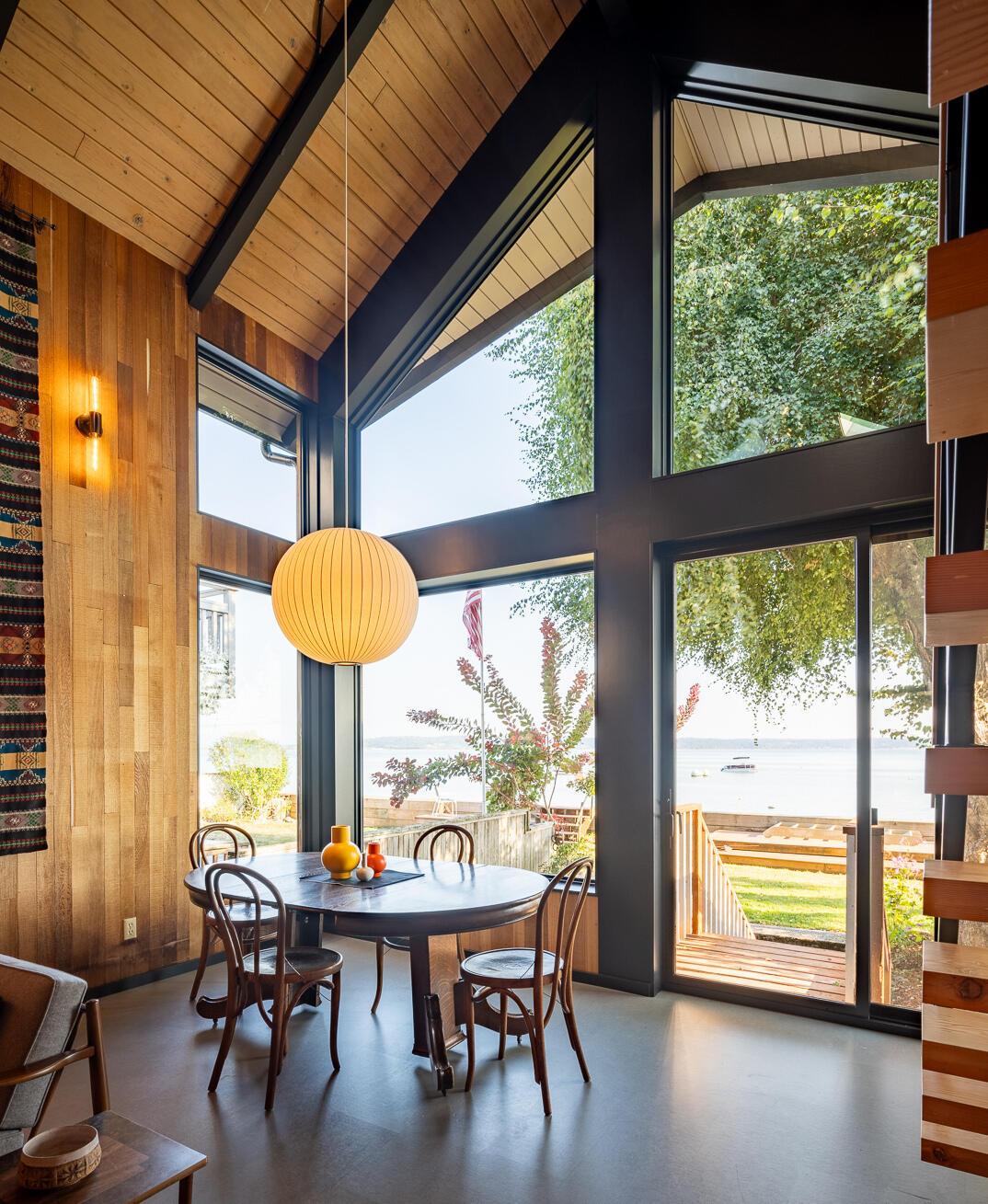 El comedor fluye perfectamente hacia la gran sala. La decoración minimalista y el enfoque en la luz natural crean un telón de fondo tranquilo y acogedor para comidas y reuniones familiares. Gracias a la estructura elevada y al nuevo marco de acero, las vistas de Puget Sound están sin obstáculos. Cuatro ventanas más grandes reemplazaron las antiguas seis pequeñas aberturas, lo que hace que la cabina se sienta conectada con el entorno junto al agua y, al mismo tiempo, garantiza la seguridad contra inundaciones.