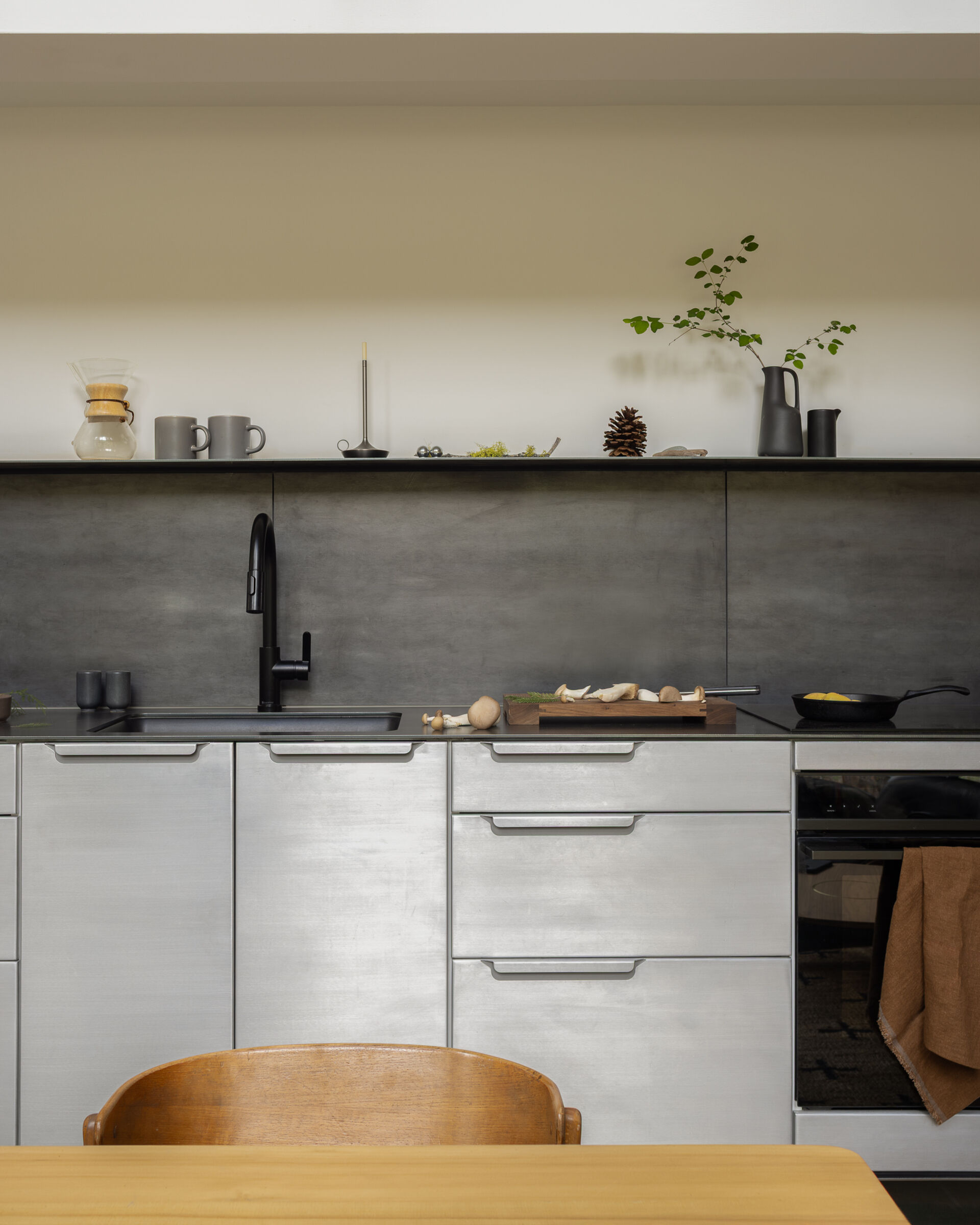 The kitchen is defined by raw steel countertops and a matching backsplash, both fabricated by the owner, giving the space a direct and utilitarian character. Aluminum kitchen casework keeps the layout efficient, while wall-mounted sconces provide focused task lighting.