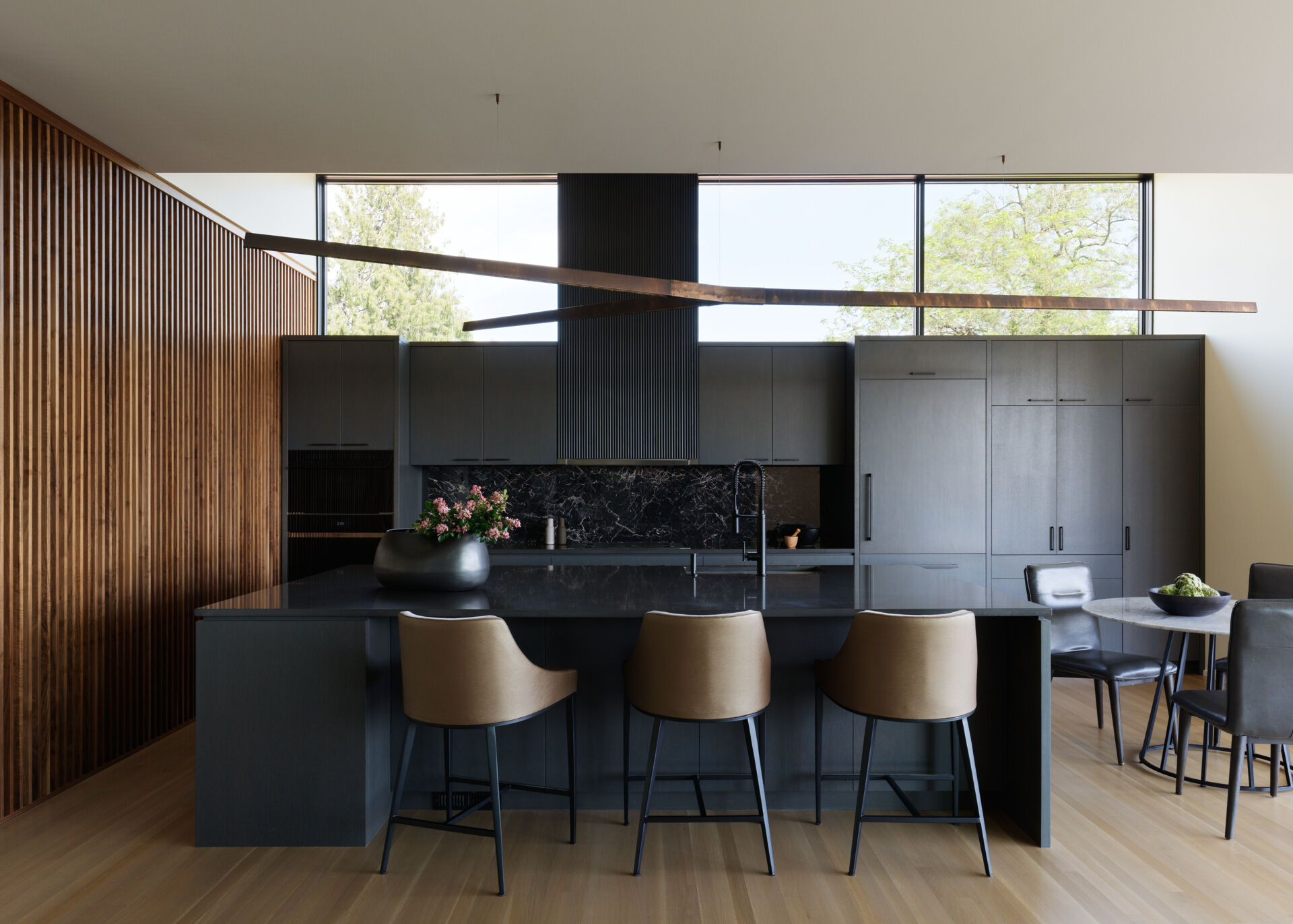 In this kitchen, charcoal quartz countertops and a black marble backsplash shine in natural light, while dark-stained cabinetry adds sleek, reflective elegance.