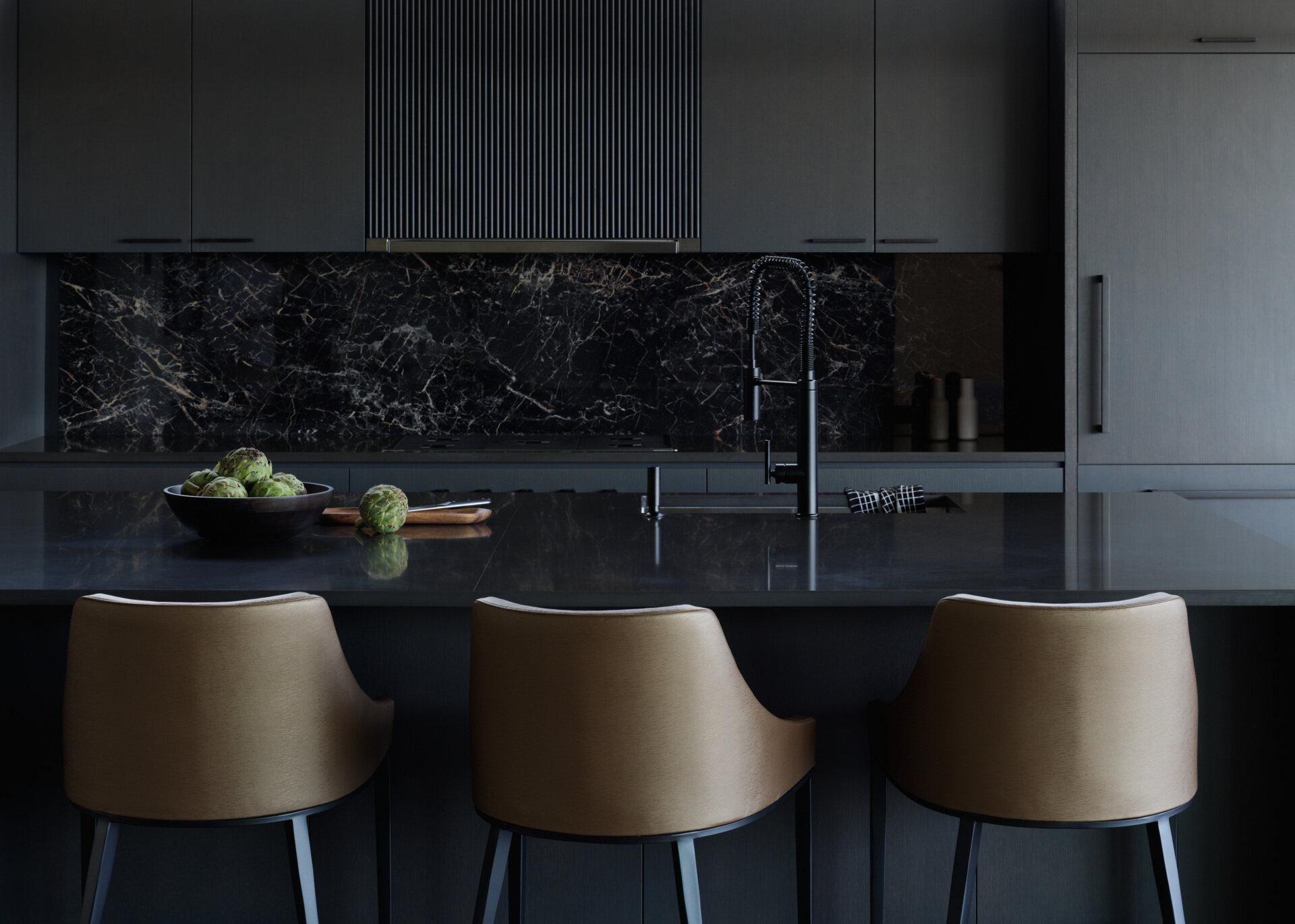 In this kitchen, charcoal quartz countertops and a black marble backsplash shine in natural light, while dark-stained cabinetry adds sleek, reflective elegance.