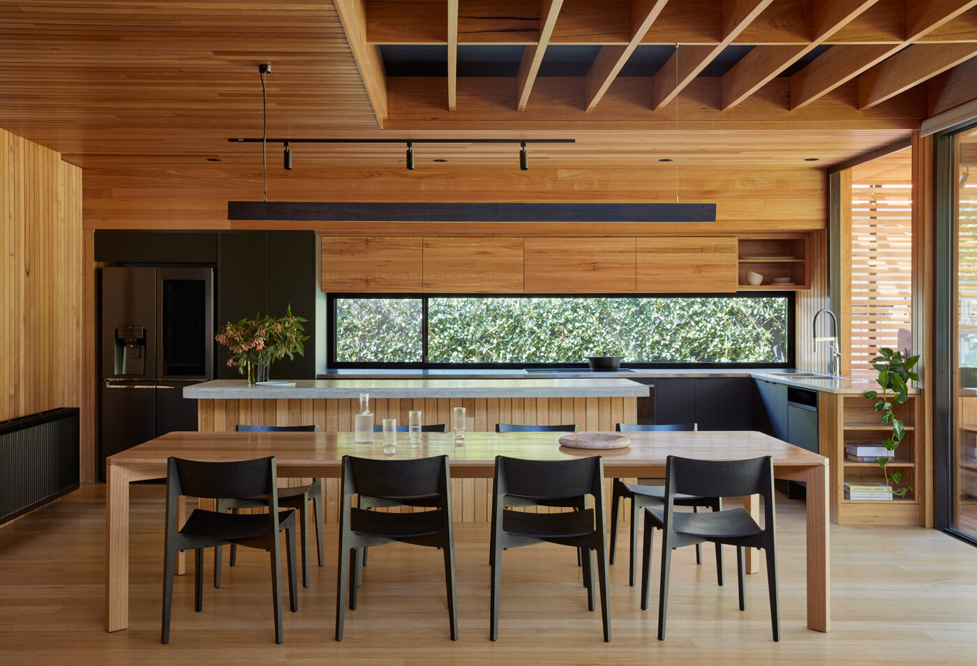 Los nuevos espacios de sala, comedor y cocina forman el núcleo de la extensión. La calidez proviene del respaldo de fresno Vic de origen local y de las tablas del piso de roble Tasse, bañadas por una luz natural en constante cambio. Una lámpara de araña hecha a mano con vigas de techo recuperadas aporta historia al nuevo espacio, mientras que los gabinetes negros y de madera en la cocina se alinean en las paredes y los bancos de concreto en el lugar introducen un contrapunto táctil y conectado a tierra.