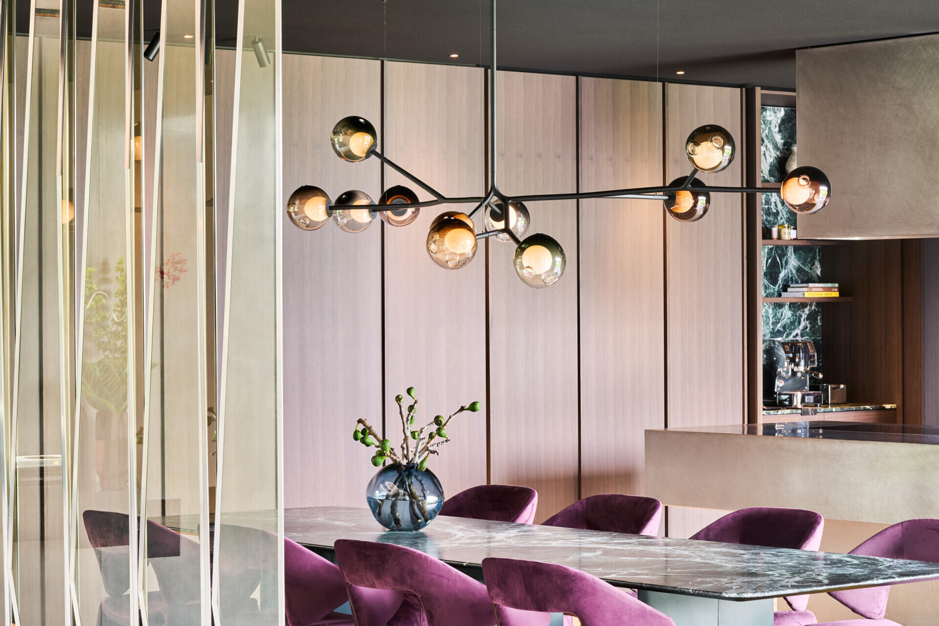 This dining space balances soft elegance with a little sparkle. A smoky-glass globe chandelier stretches above the stone table top, while plush plum velvet chairs add rich texture and comfort.
