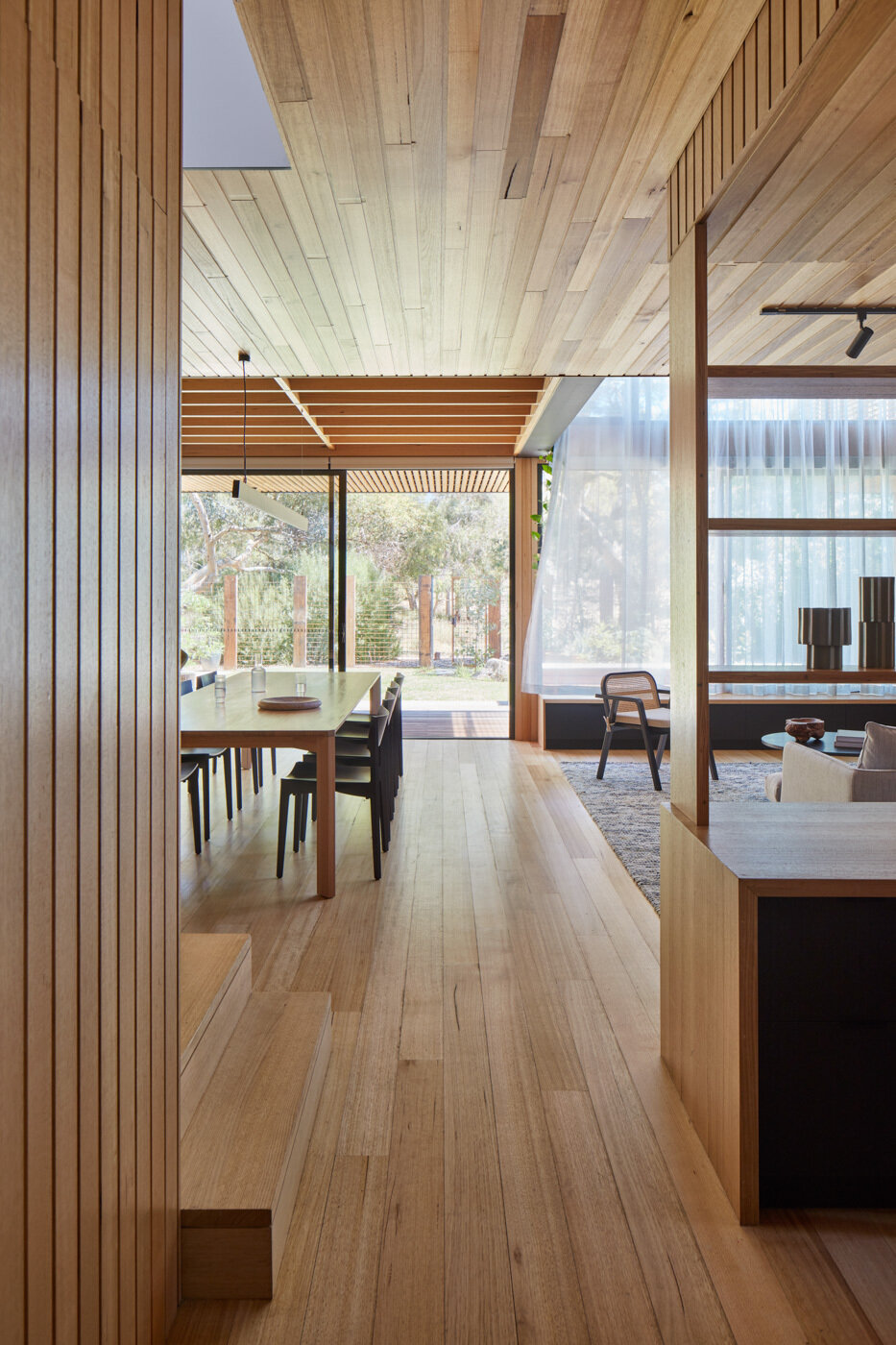 Los nuevos espacios de sala, comedor y cocina forman el núcleo de la extensión. La calidez proviene del respaldo de fresno Vic de origen local y de las tablas del piso de roble Tasse, bañadas por una luz natural en constante cambio. Una lámpara de araña hecha a mano con vigas de techo recuperadas aporta historia al nuevo espacio, mientras que los gabinetes negros y de madera en la cocina se alinean en las paredes y los bancos de concreto en el lugar introducen un contrapunto táctil y conectado a tierra.