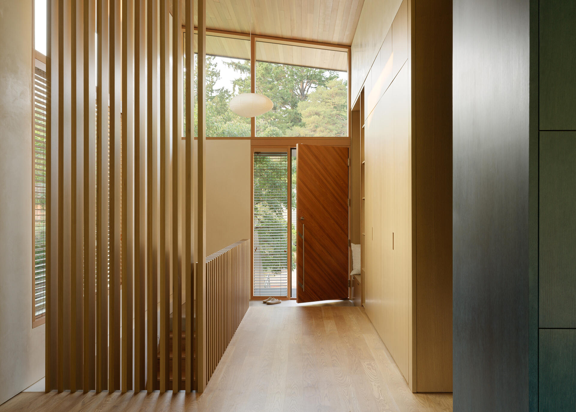 A recessed Japanese-style entry welcomes residents with a built-in wood bench and storage. White oak screens filter views and light between the entry, main stair, and living room, creating a calm transition into the home. The entry sets the tone with a simple, natural material palette and subtle contrasts.