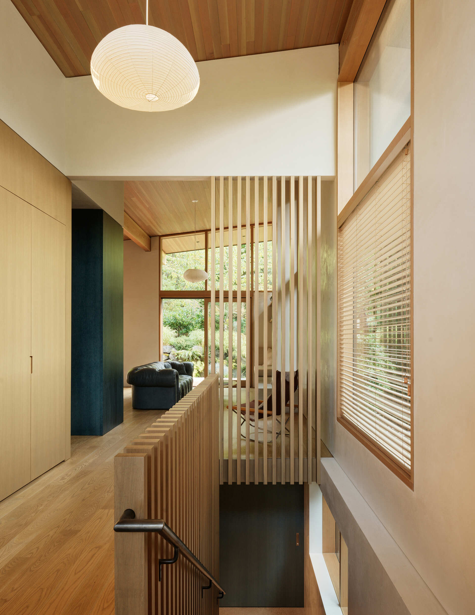 A recessed Japanese-style entry welcomes residents with a built-in wood bench and storage. White oak screens filter views and light between the entry, main stair, and living room, creating a calm transition into the home. The entry sets the tone with a simple, natural material palette and subtle contrasts.