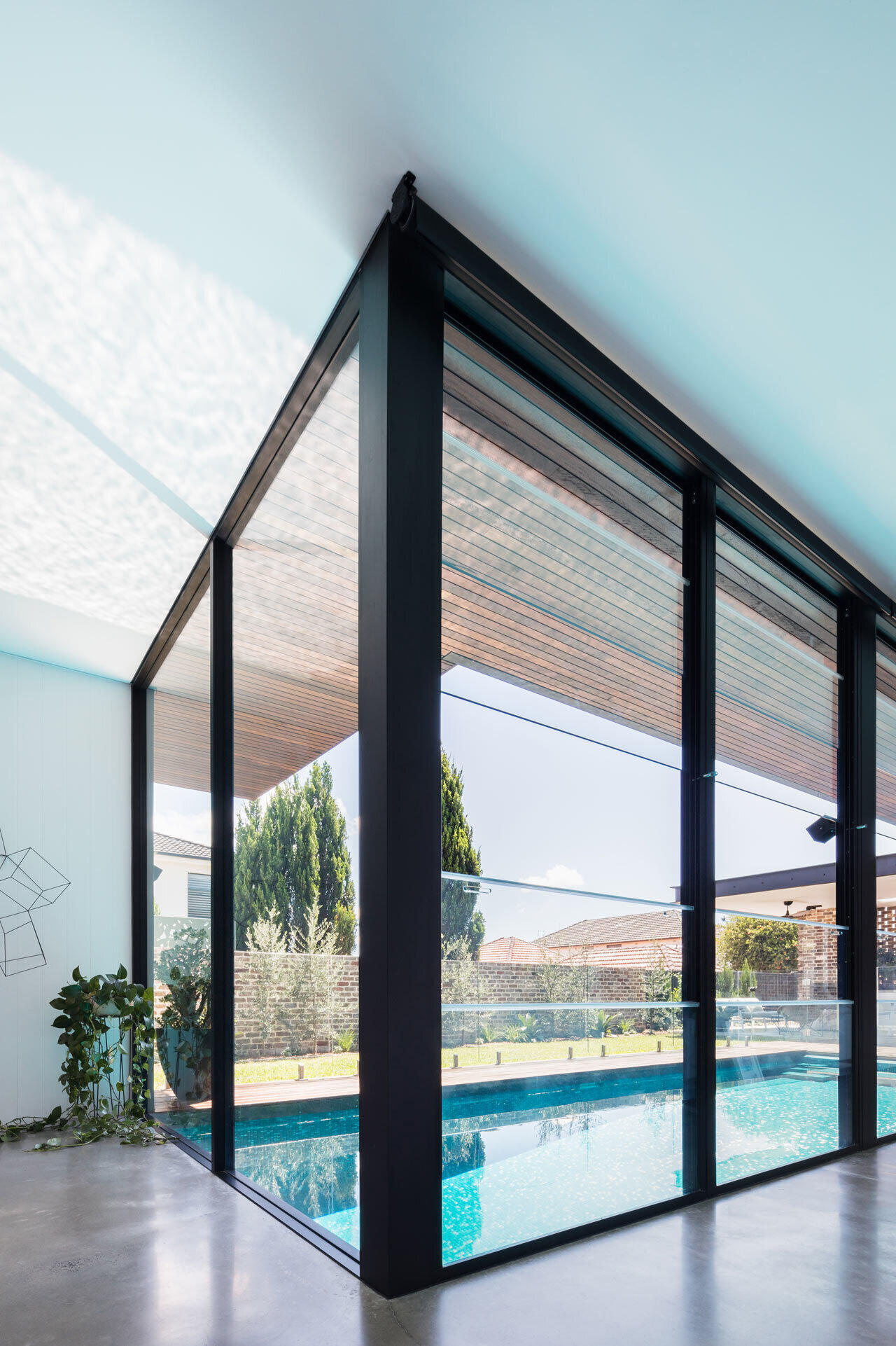 Floor-to-ceiling black-framed windows flood the home with natural light and frame views of the pool.