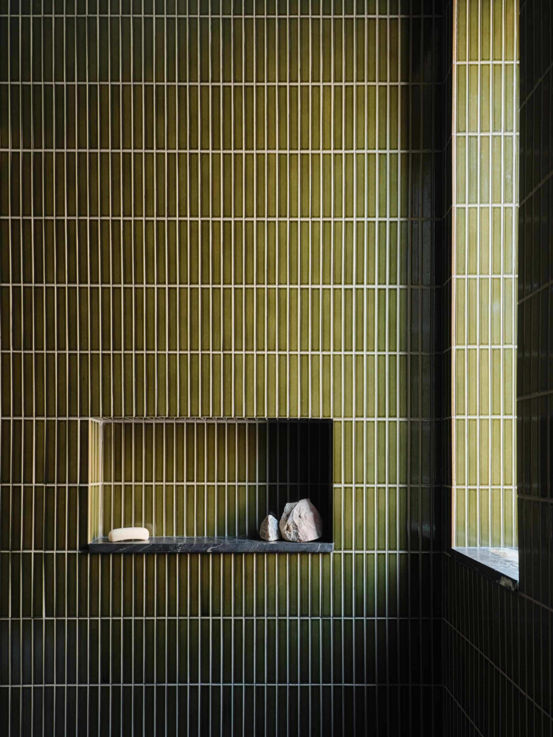 The guest bathroom is lined with forest green Japanese tile. The material choice brings depth and contrast into a small, controlled space.