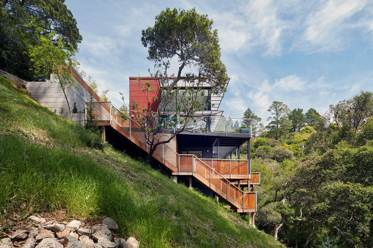 A weathering steel hillside house in Mill Valley hides a bright yellow door and opens into a light-filled home with floating stairs, double height living and forest views.