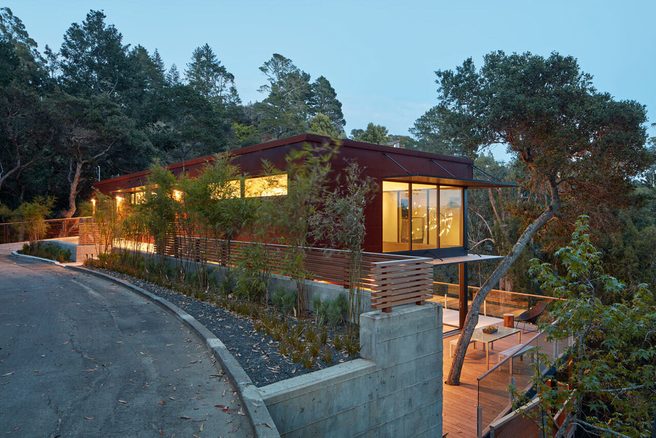Una casa de acero corten en la ladera de una colina en Mill Valley oculta una puerta de color amarillo brillante que conduce a una casa llena de luz con una escalera flotante, una sala de estar de doble altura y vistas al bosque.