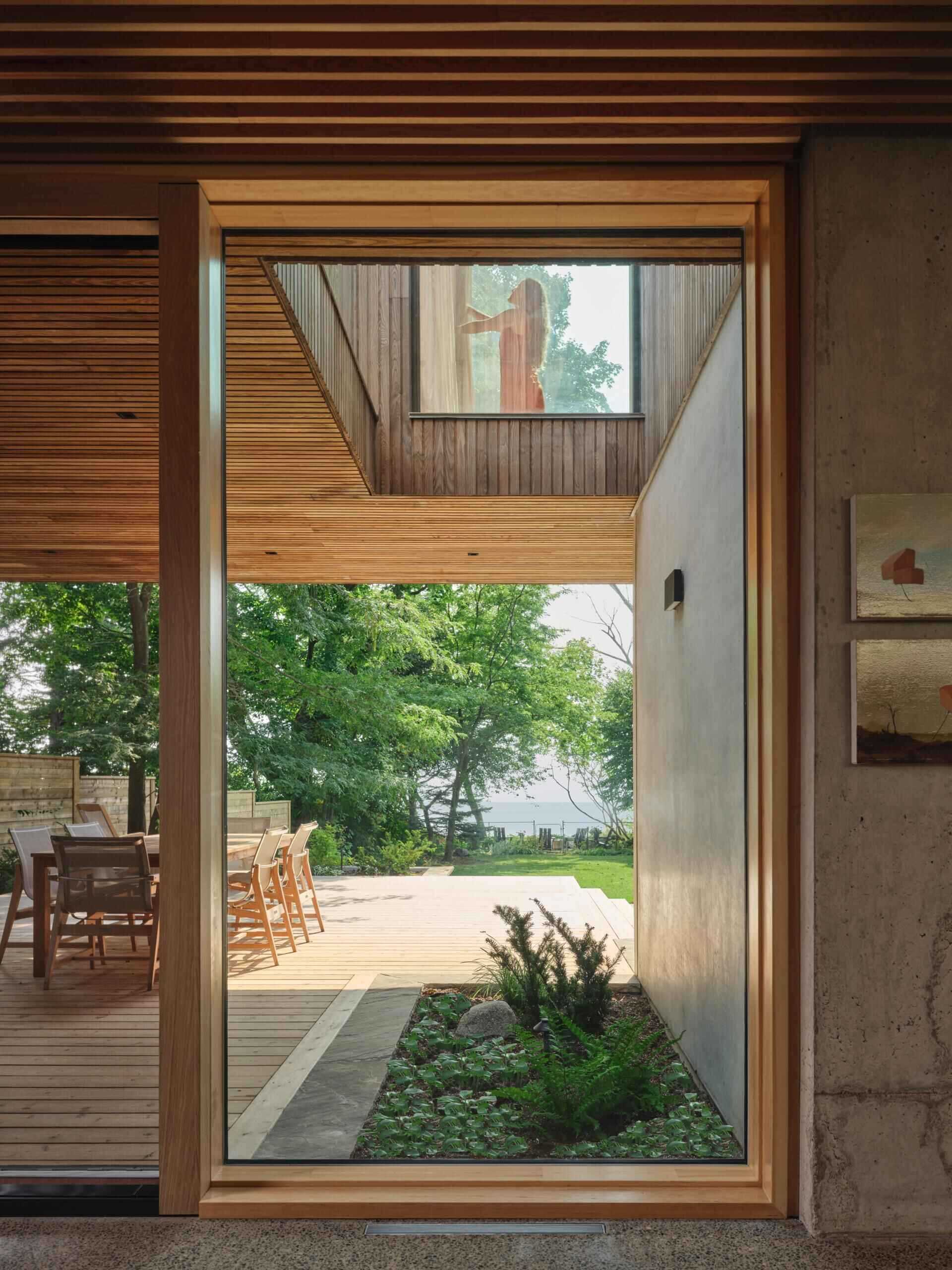 The kitchen sits within the concrete framework, unified with the living room by a Douglas Fir ceiling. Oak millwork reinforces the continuity between spaces while remaining clearly inserted into the structural shell. From here, views extend south toward Lake Ontario, with light shaping both movement and pause within the room.