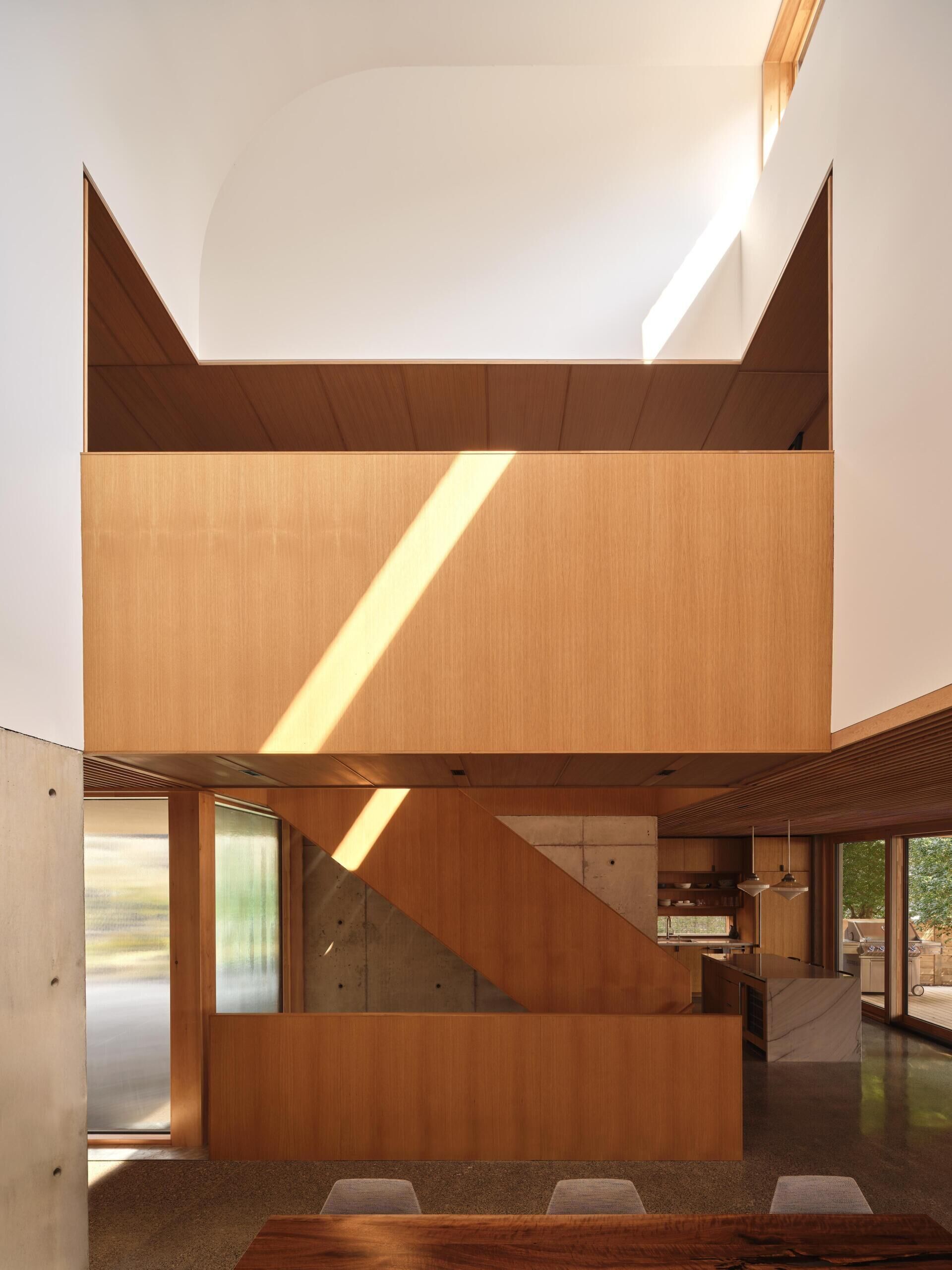 This dining room is defined by a soaring 26-foot-tall ceiling. A south-facing light monitor draws daylight down through the volume, creating height without increasing floor area.