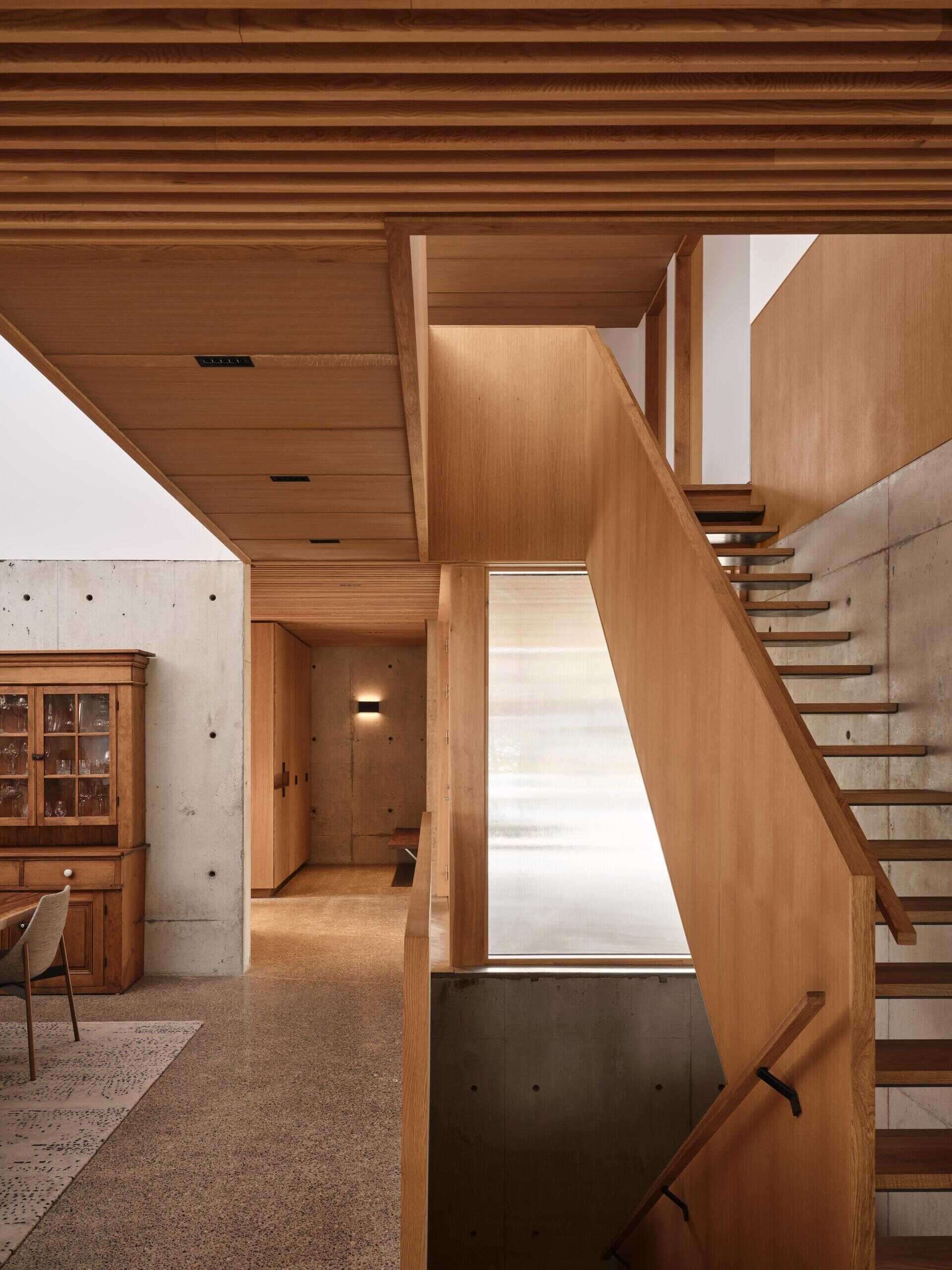 Entry occurs beneath the front cantilever, compressing the experience before opening inward. A reeded glass door brings daylight into the entry while maintaining privacy along the closely spaced street. Concrete anchors the service core here, performing as structure, shoring, and thermal mass. Wood millwork lines circulation and primary rooms, establishing a tactile contrast to the raw concrete.