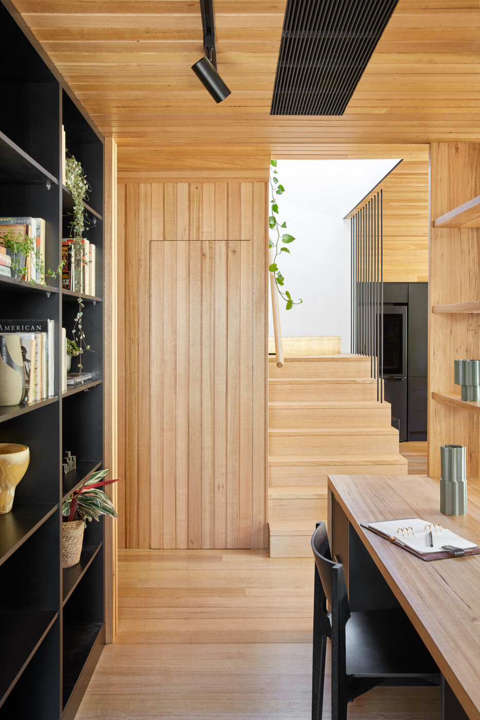 El rincón de estudio en el primer piso está parcialmente rodeado por estanterías, lo que proporciona un equilibrio entre concentración y conexión. Está ubicado dentro de un espacio que se puede abrir que permite trabajar desde casa, manteniendo la conexión visual con el espacio habitable y las vistas más allá, mientras que las particiones brindan separación sin aislar.