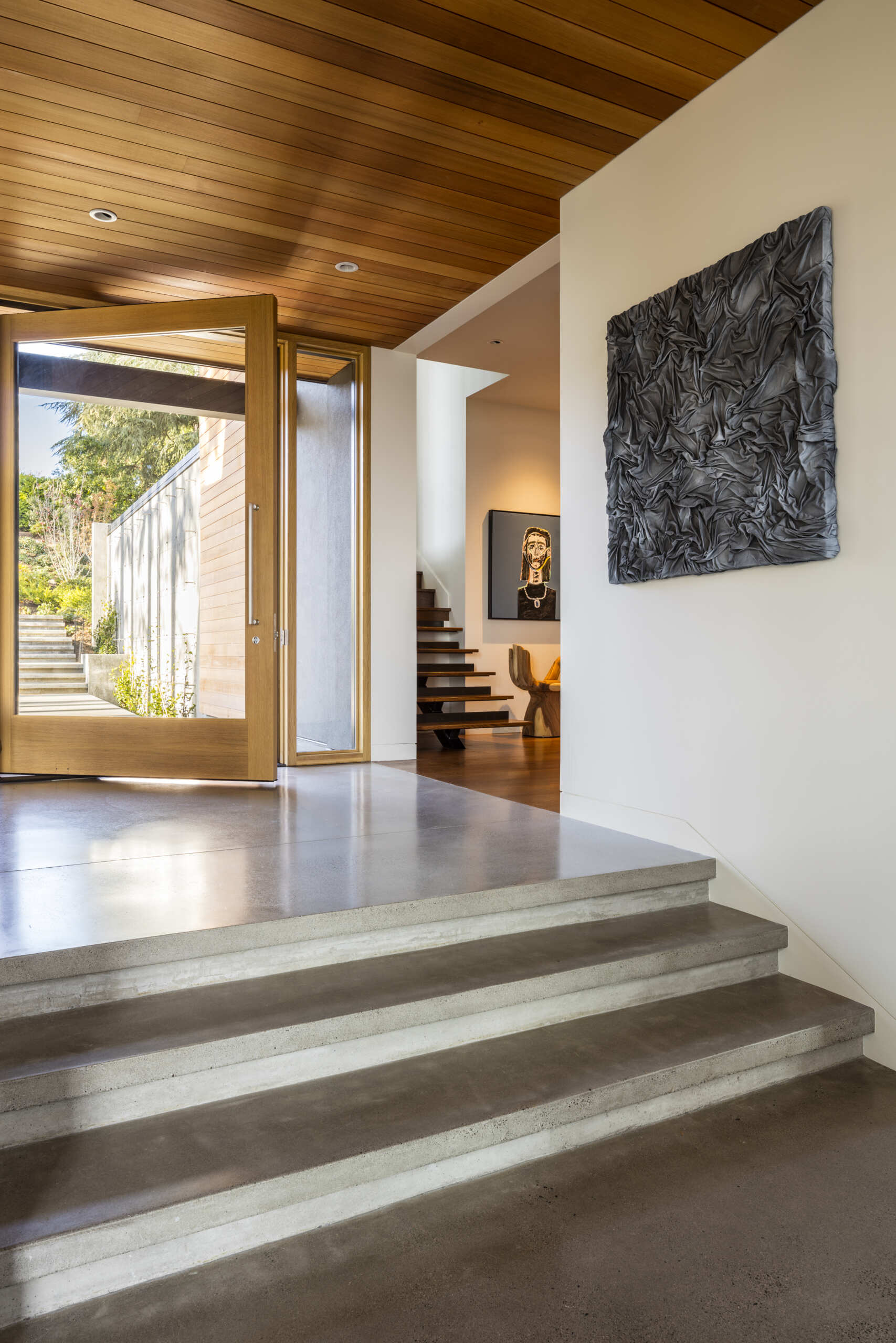 A landscaped courtyard carved into the hillside leads to an oversized pivot door, creating a calm transition from street to home.