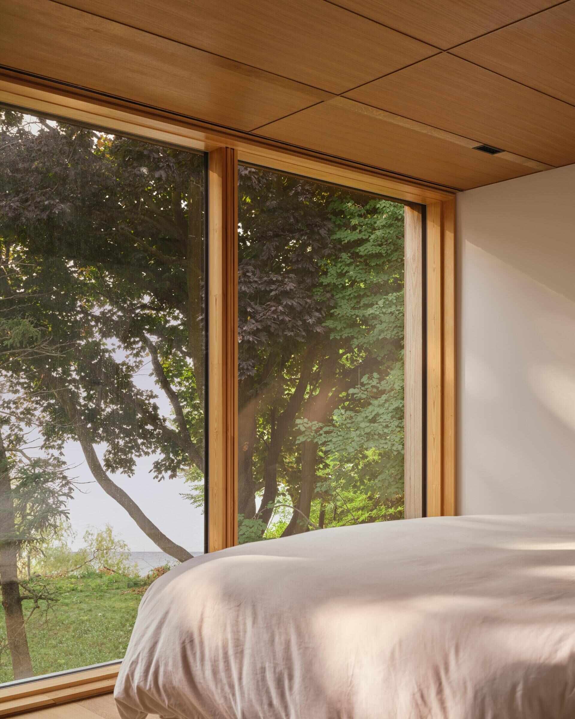 The primary bedroom, with a wood-line ceiling, faces the lake, opening to expansive views of Lake Ontario. It connects directly to the second-floor deck, sharing light, air, and sky.