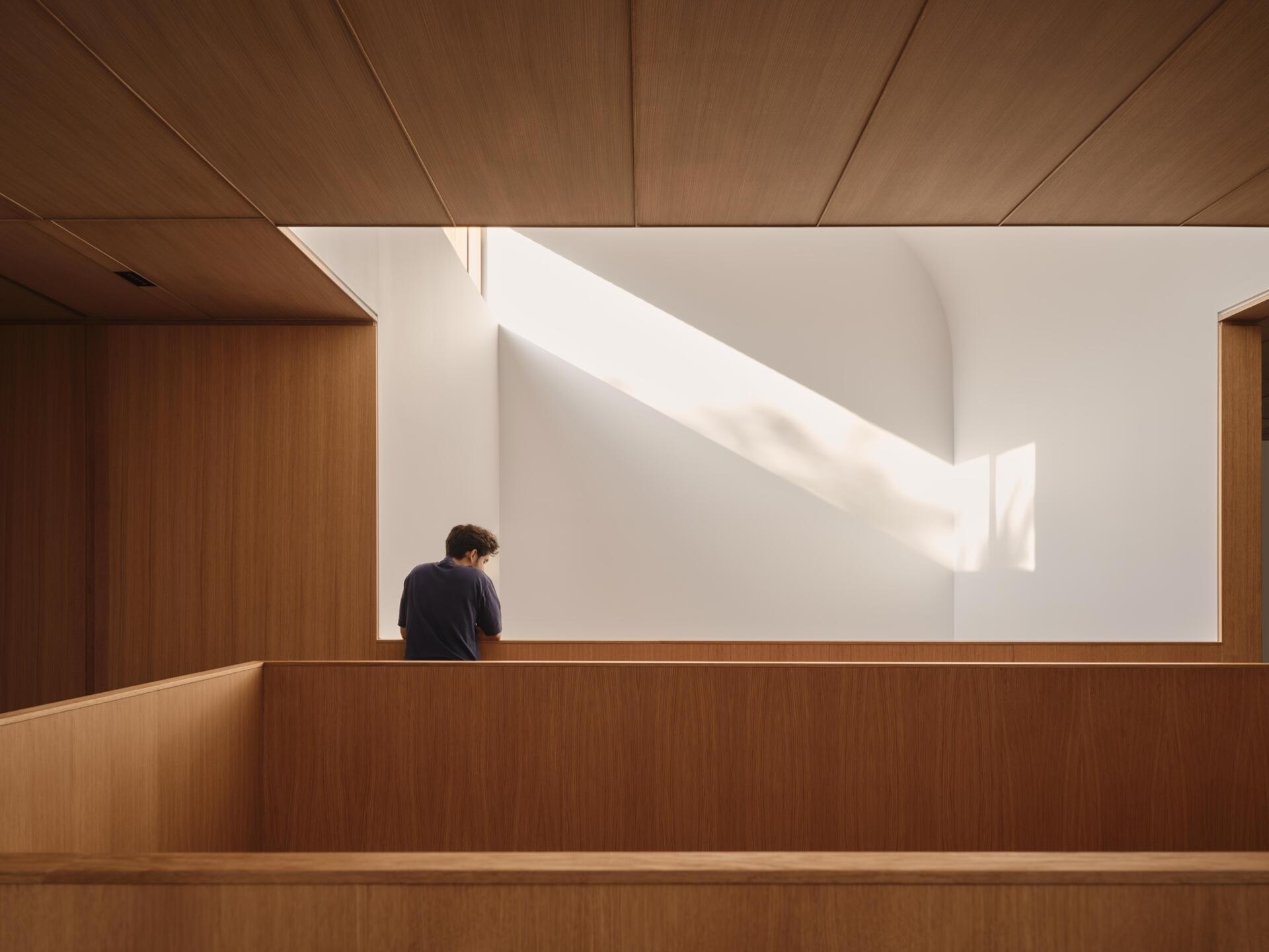 The stair flanks the central service zone, acting as both circulation and connector. Above, the stair participates in the vertical sequence created by the light monitors, tying together spaces above and below.