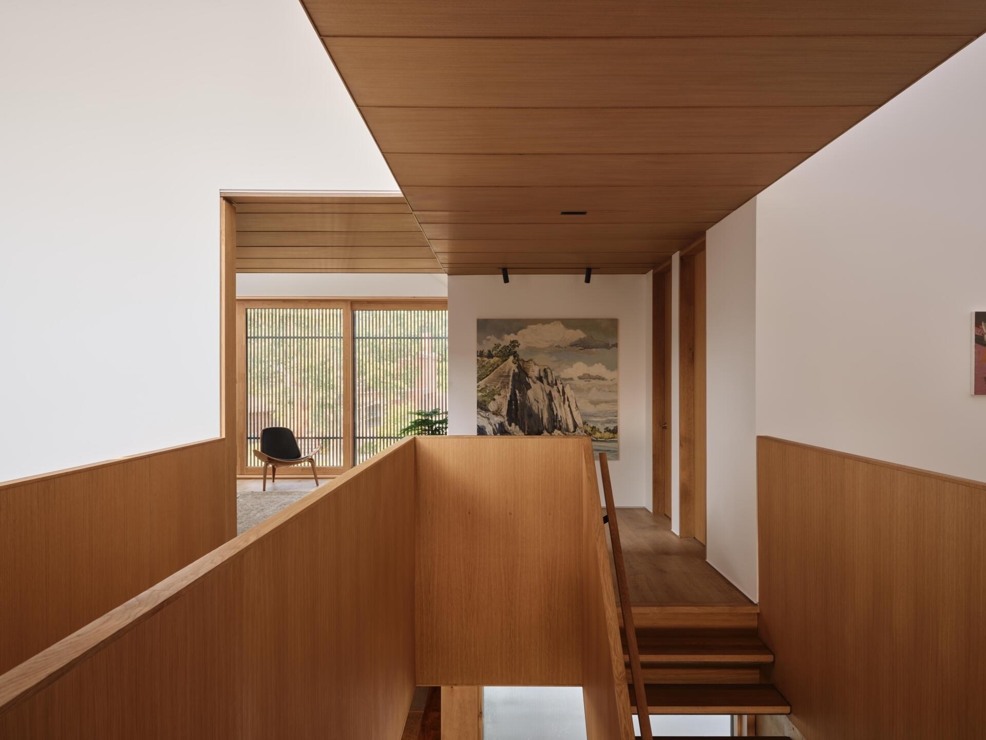 The stair flanks the central service zone, acting as both circulation and connector. Above, the stair participates in the vertical sequence created by the light monitors, tying together spaces above and below.