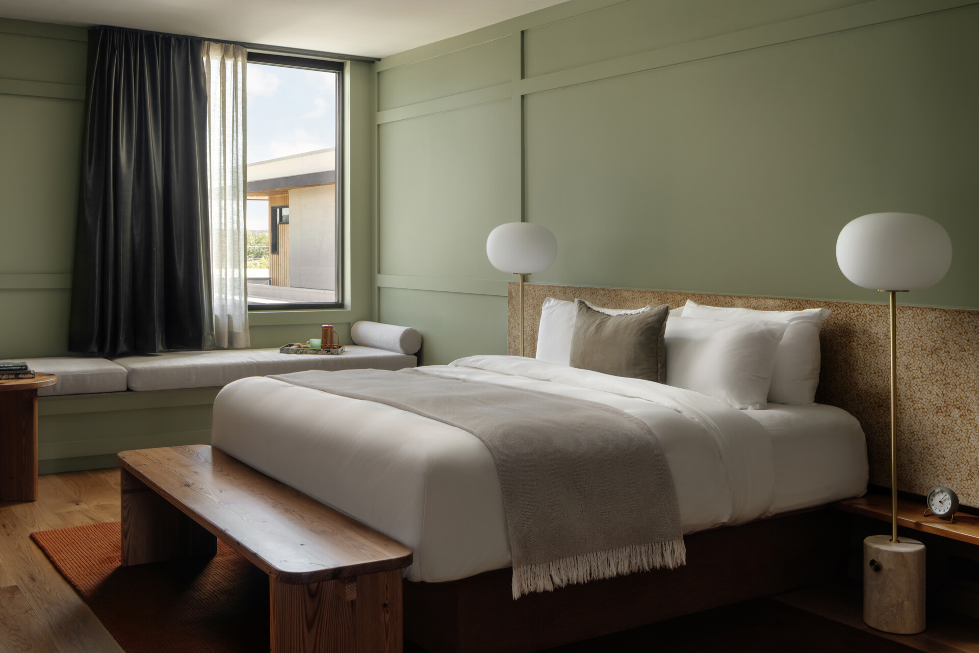 This modern hotel suites features muted green walls and matching tiles, warm timber floors, and restrained furnishings that prioritize calm, texture, and light.