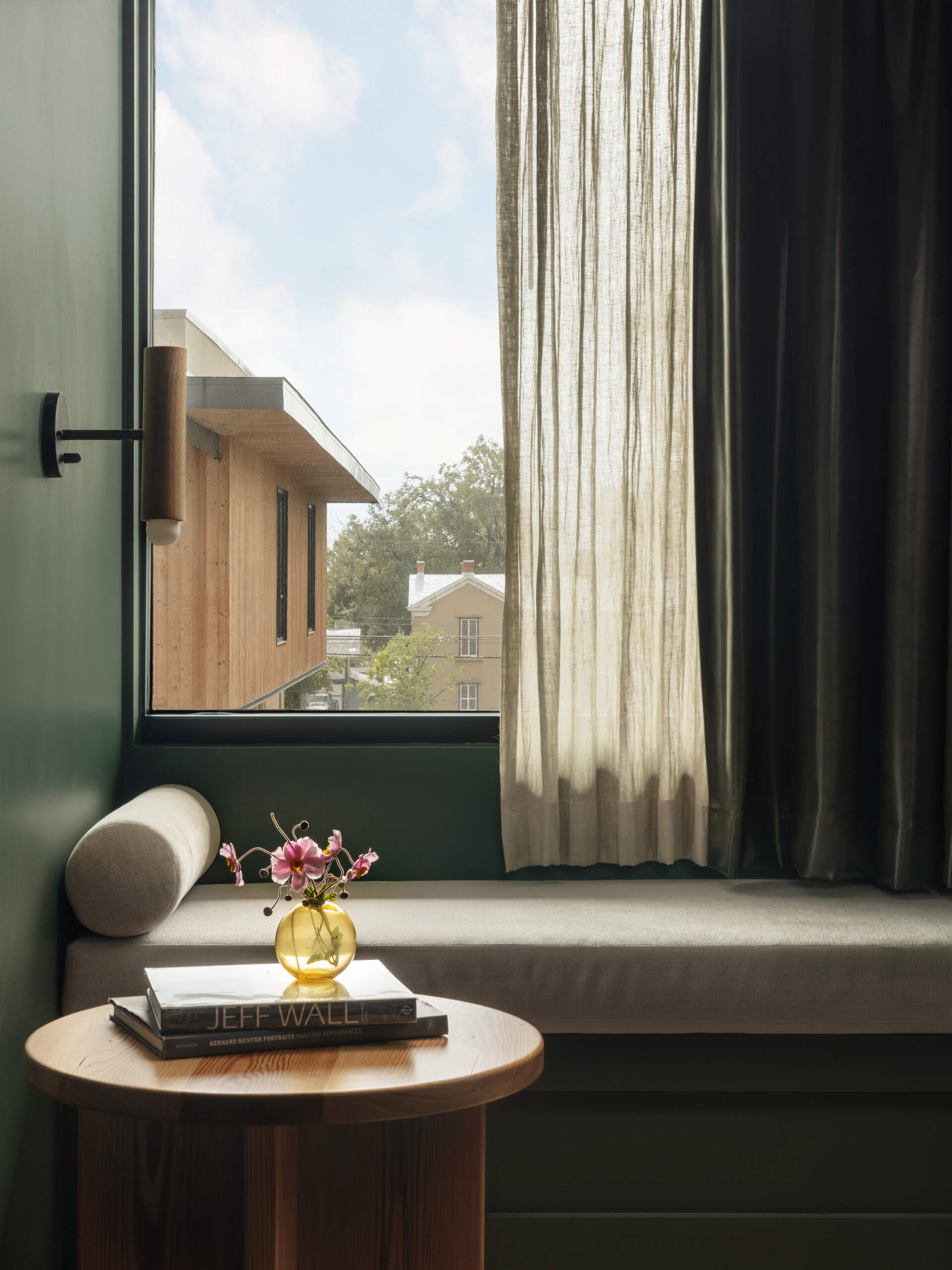 This modern hotel suites features muted green walls and matching tiles, warm timber floors, and restrained furnishings that prioritize calm, texture, and light.