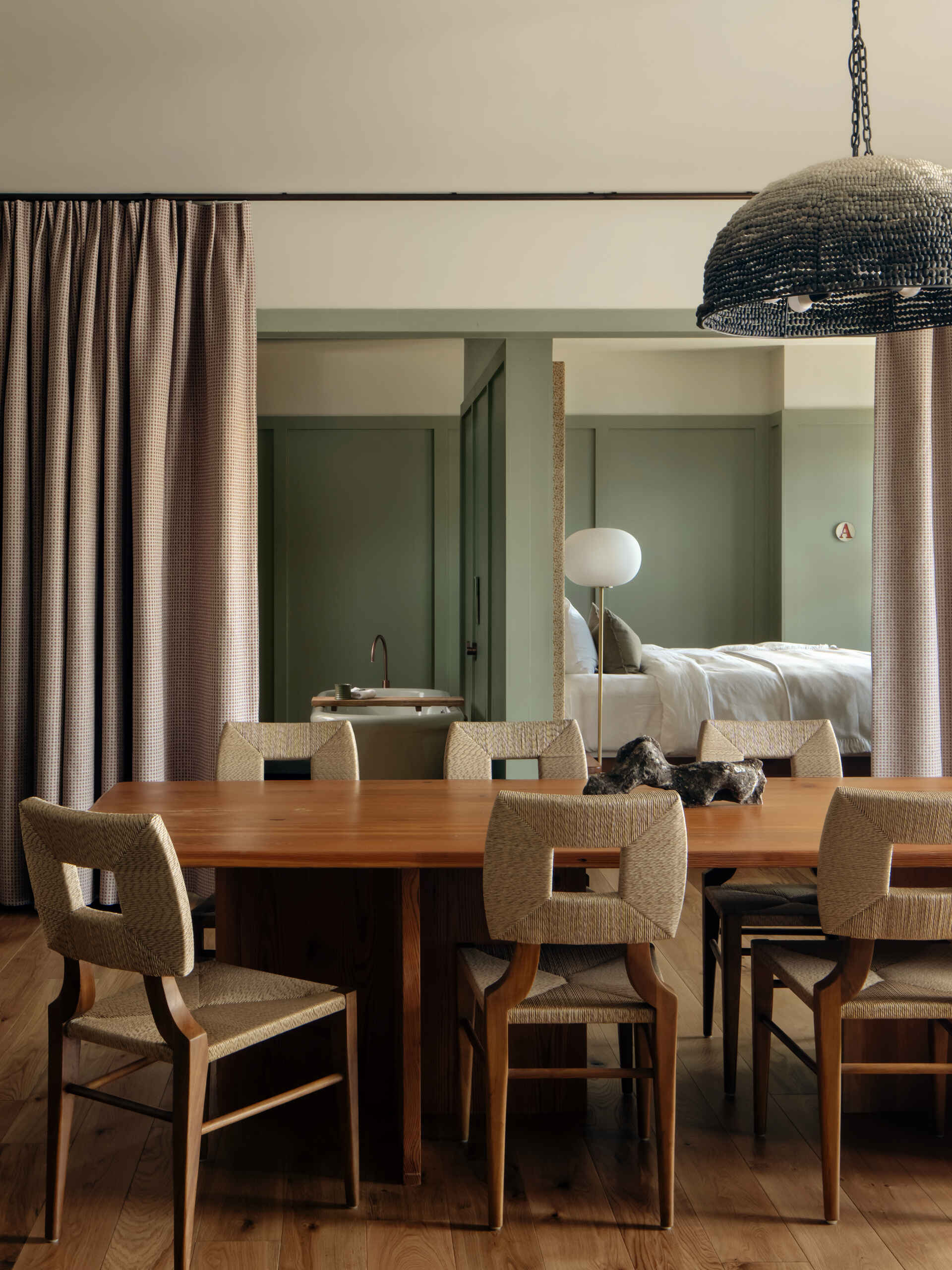 This modern hotel suites features muted green walls and matching tiles, warm timber floors, and restrained furnishings that prioritize calm, texture, and light.