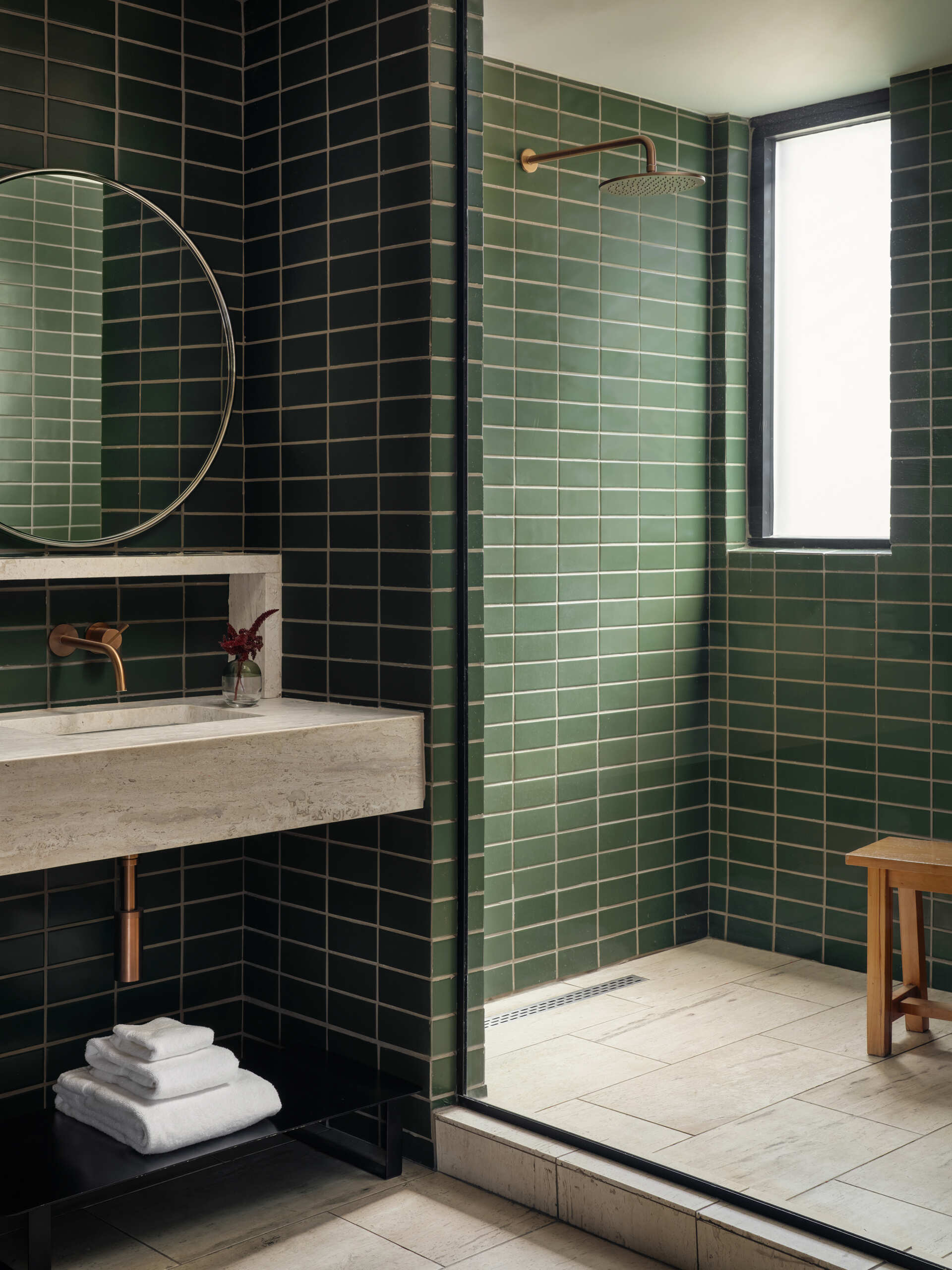 This modern hotel suites features muted green walls and matching tiles, warm timber floors, and restrained furnishings that prioritize calm, texture, and light.