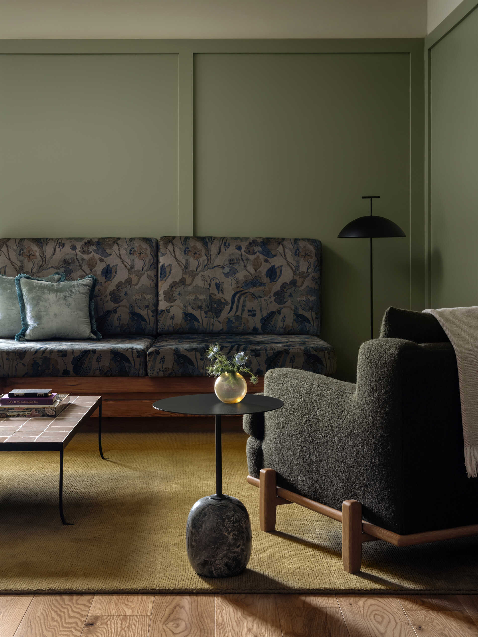 This modern hotel suites features muted green walls and matching tiles, warm timber floors, and restrained furnishings that prioritize calm, texture, and light.